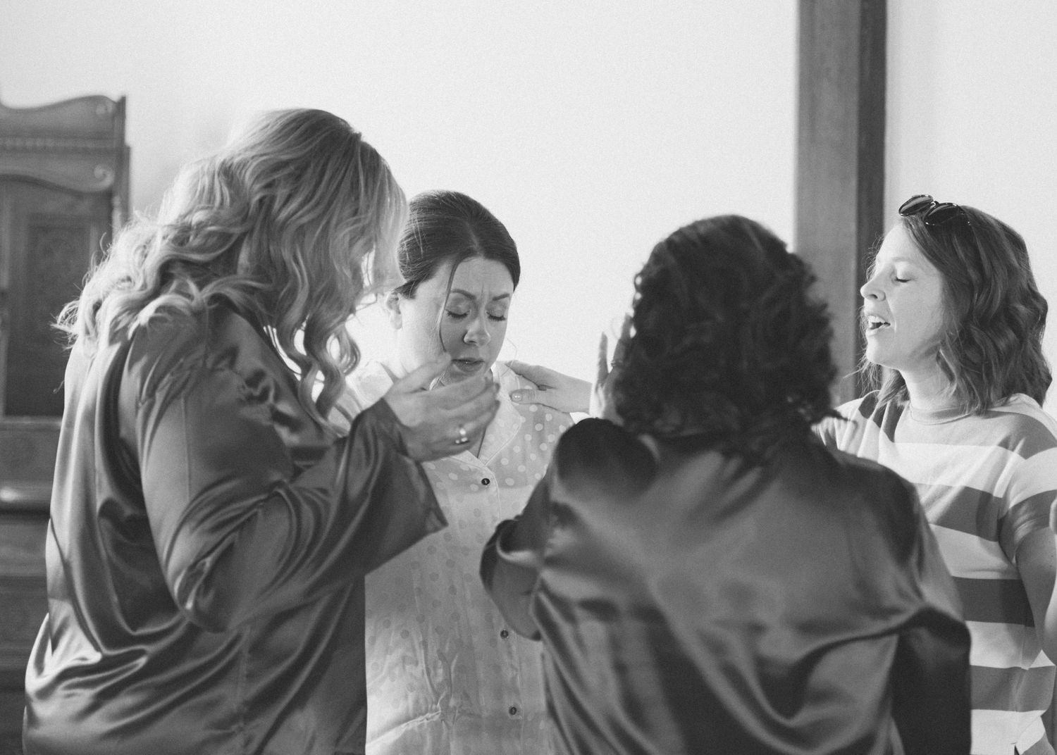 Black and white photo of bridesmaids helping bride with wedding dress preparations.