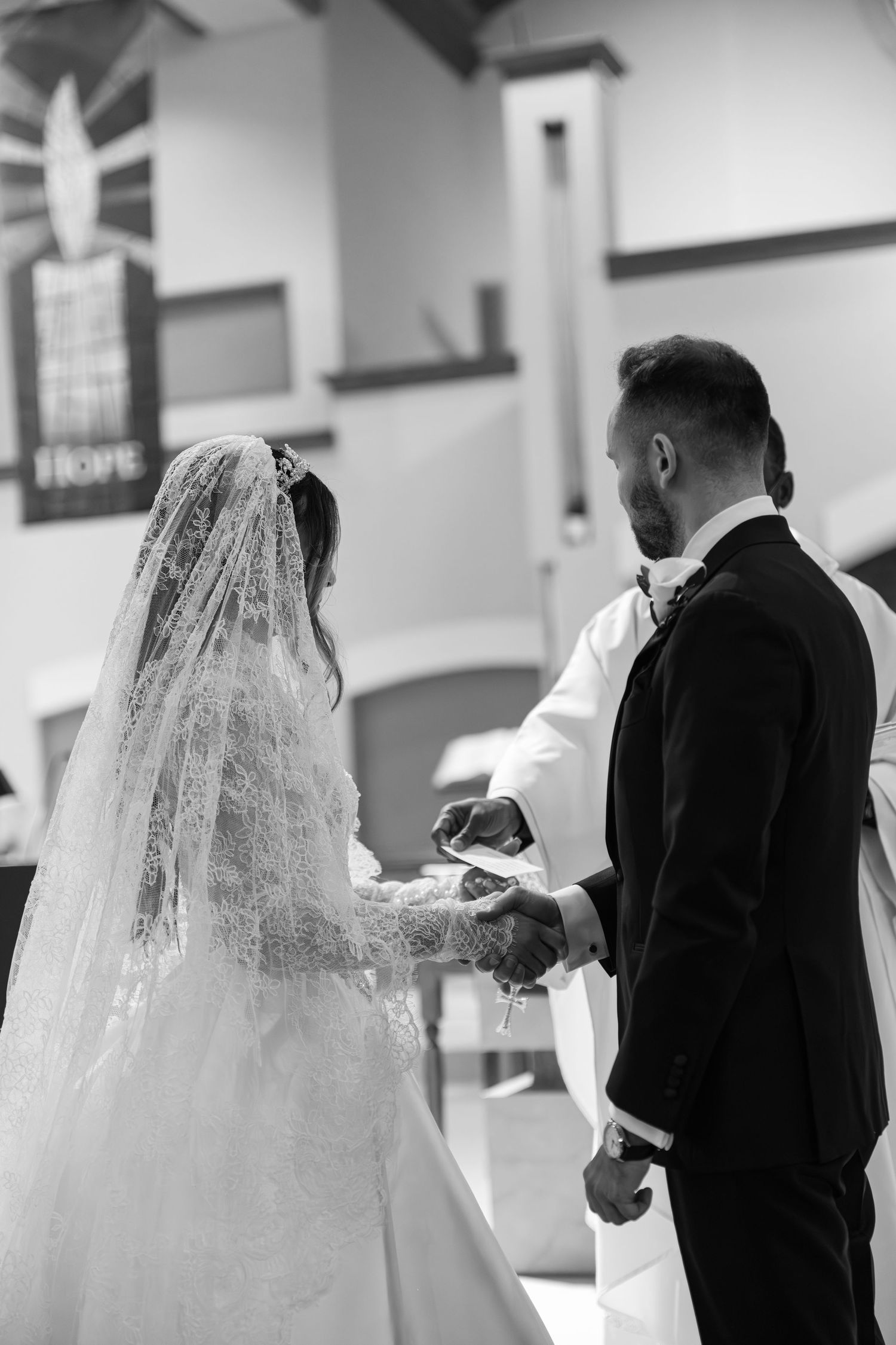 Black and white photo of bride and groom holding hands during church wedding ceremony.