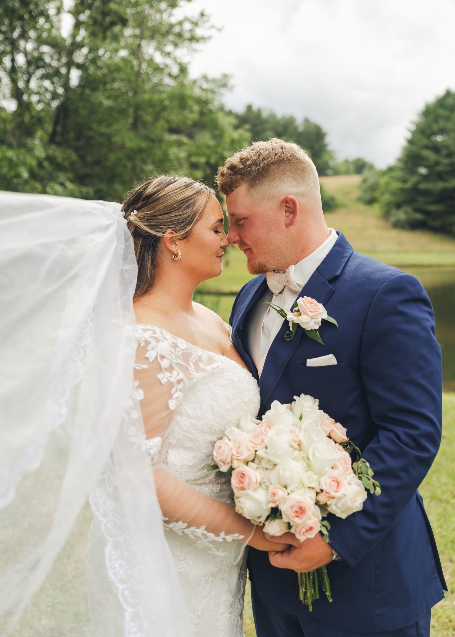 Bride and groom touch foreheads tenderly, bride holding pink and white bouquet with veil flowing.