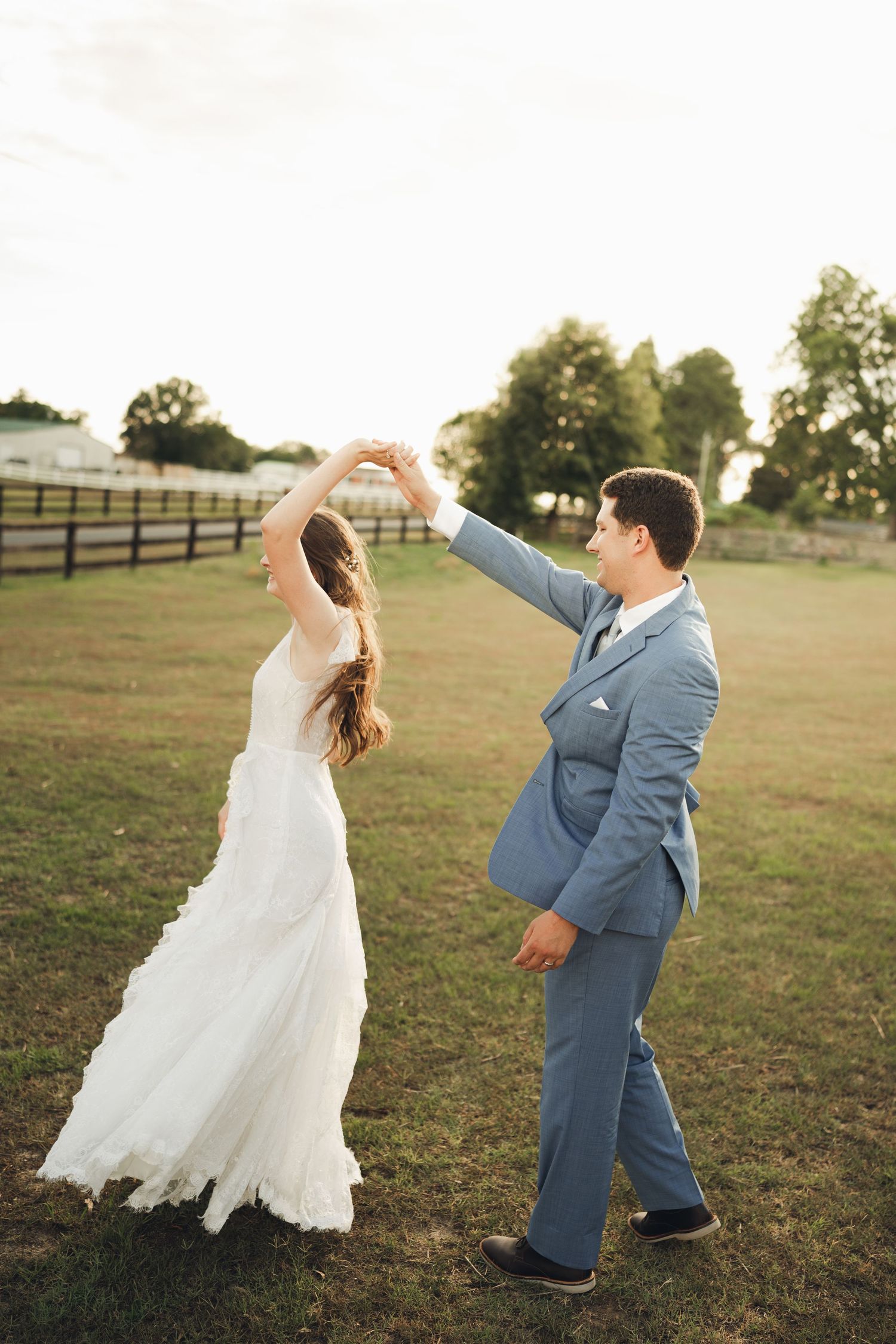 A bride and groom dance together in a green field during their outdoor farm wedding at sunset.