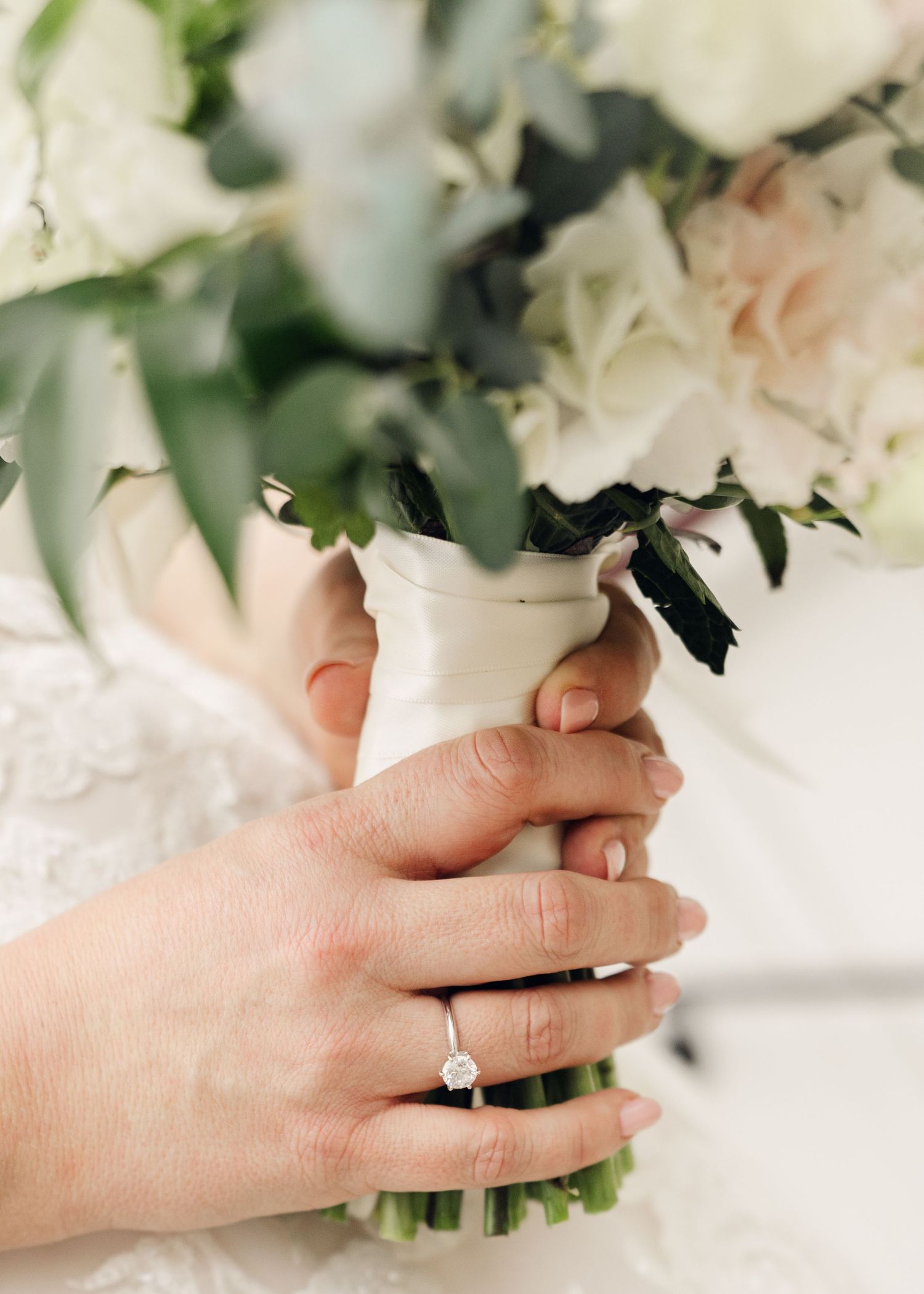 Close-up of bride holding white and green bouquet with diamond engagement ring visible.