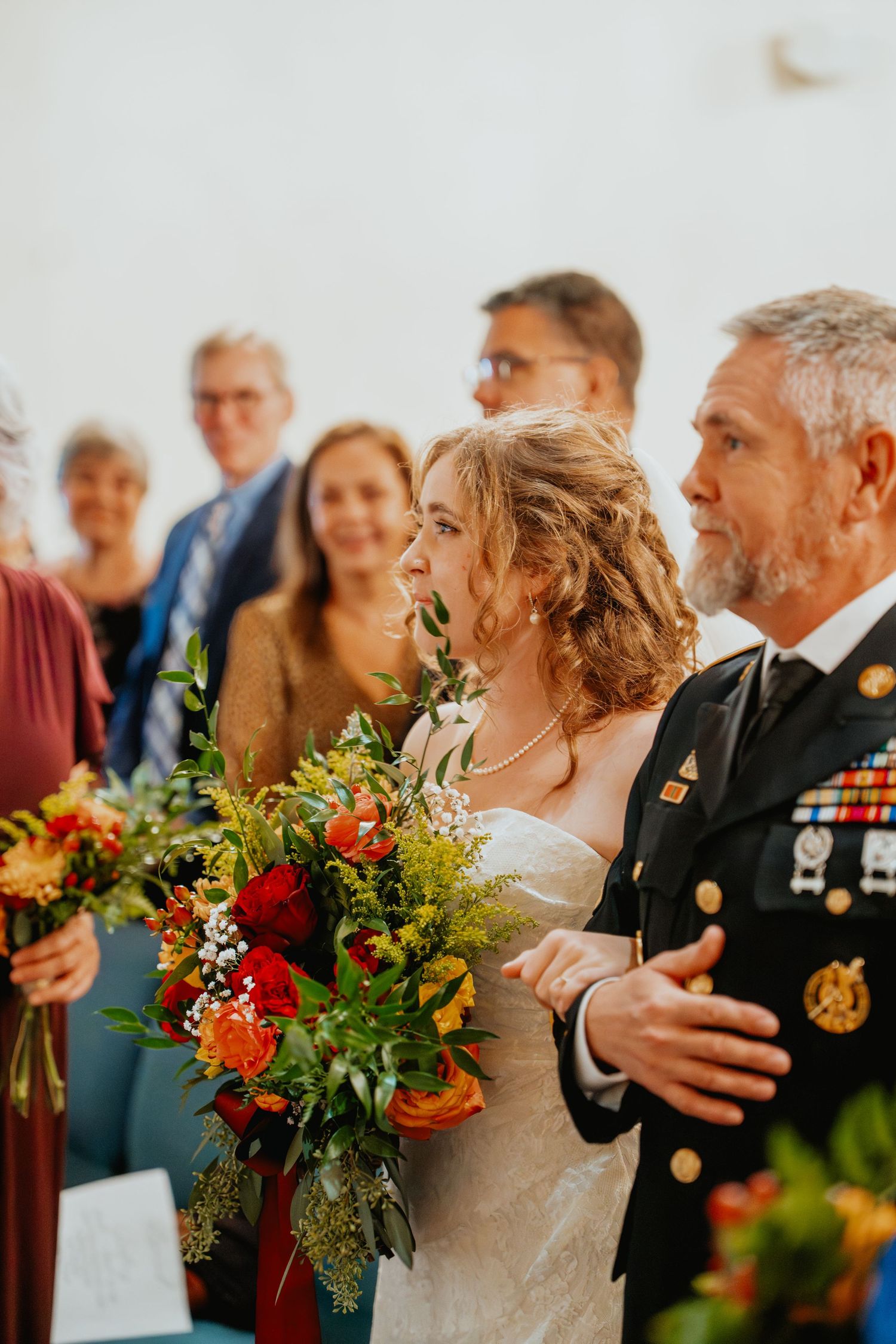 Bride walks down the aisle with a military escort holding a vibrant fall floral bouquet.