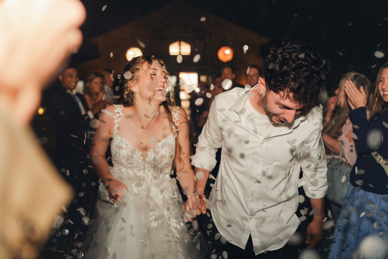 Joyful newlyweds walking through confetti shower during festive wedding celebration.
