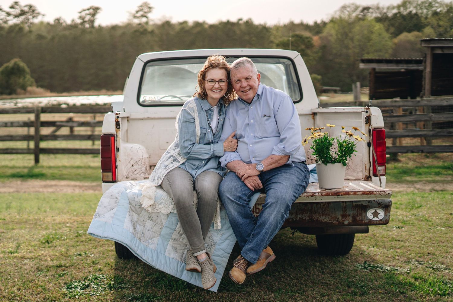 Smiling couple sitting together on tailgate of vintage white pickup truck on farm.