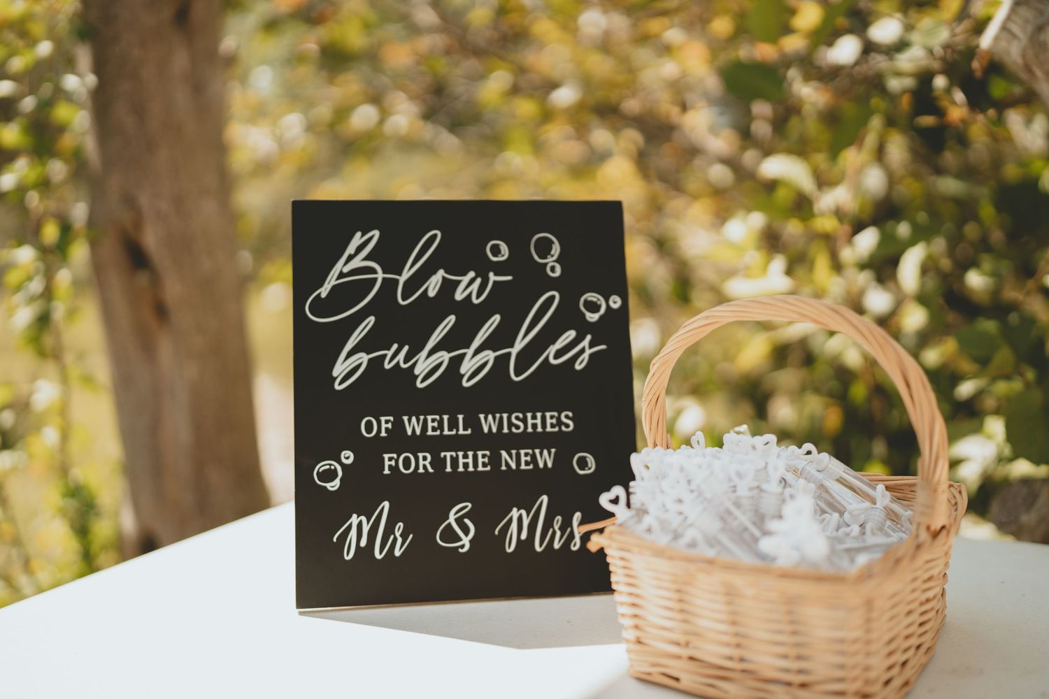 Chalkboard sign with bubble wands basket invites guests to blow bubbles for the new Mr. and Mrs.