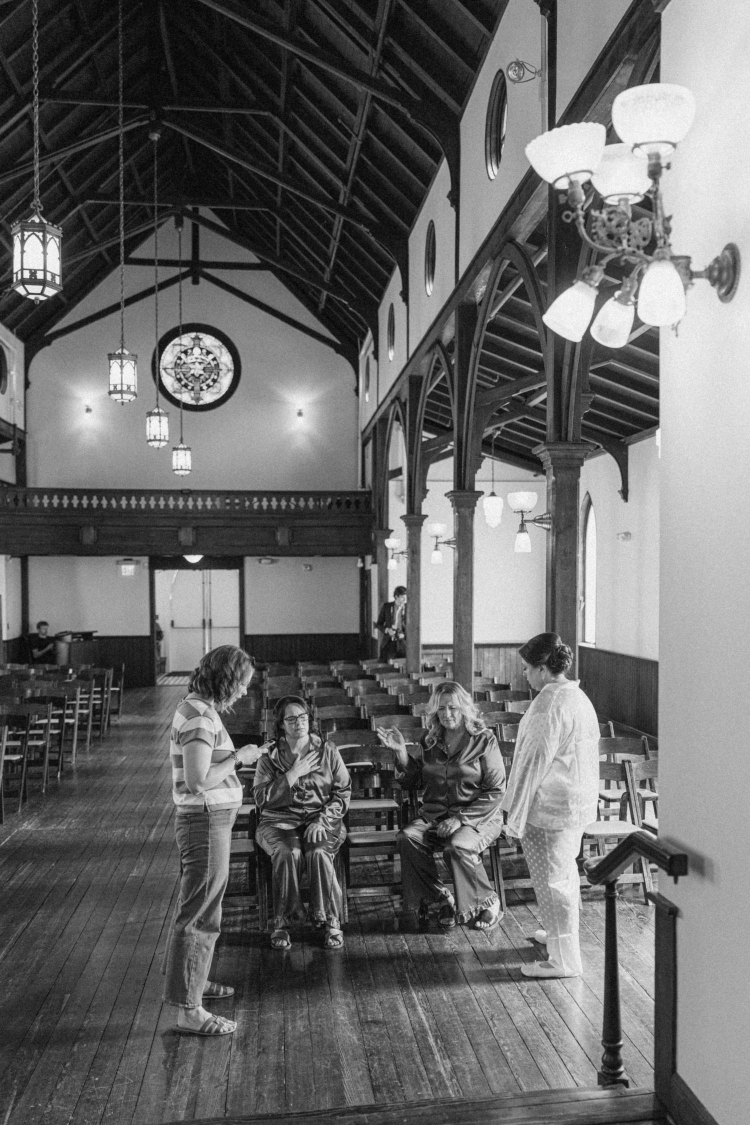 Black and white photo of guests gathering inside a historic church with vaulted wood ceilings and stained glass window.