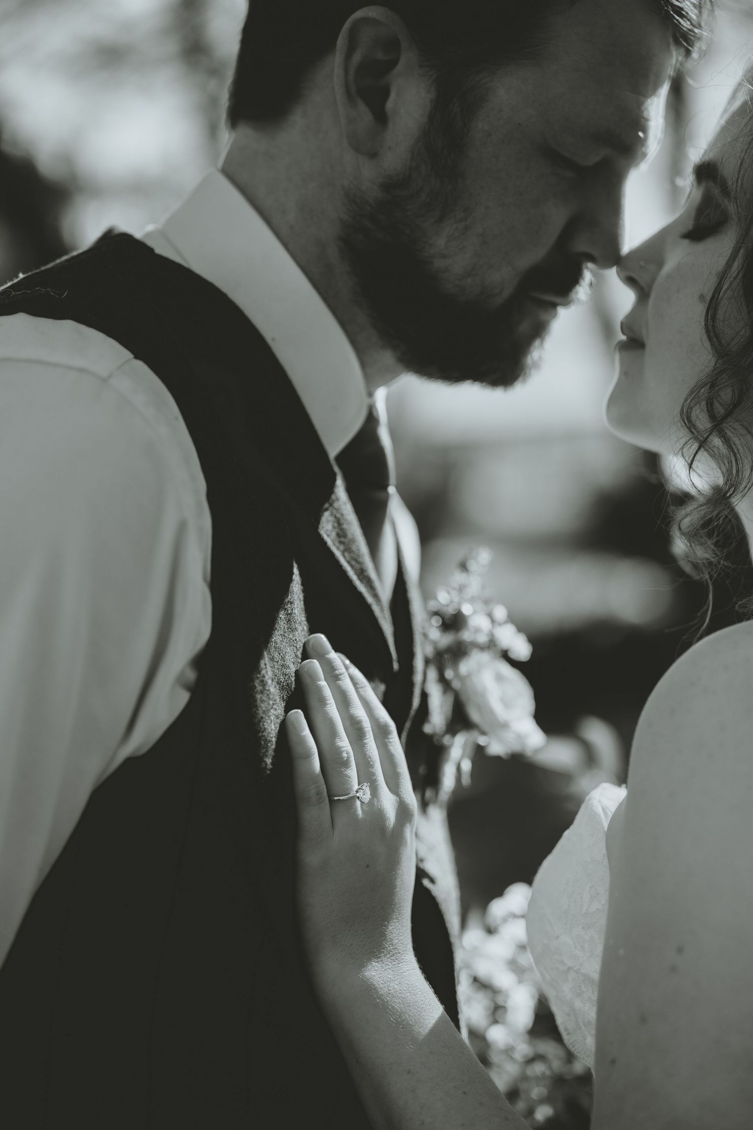 Black and white intimate moment of bride and groom nearly kissing, bride's diamond ring visible.