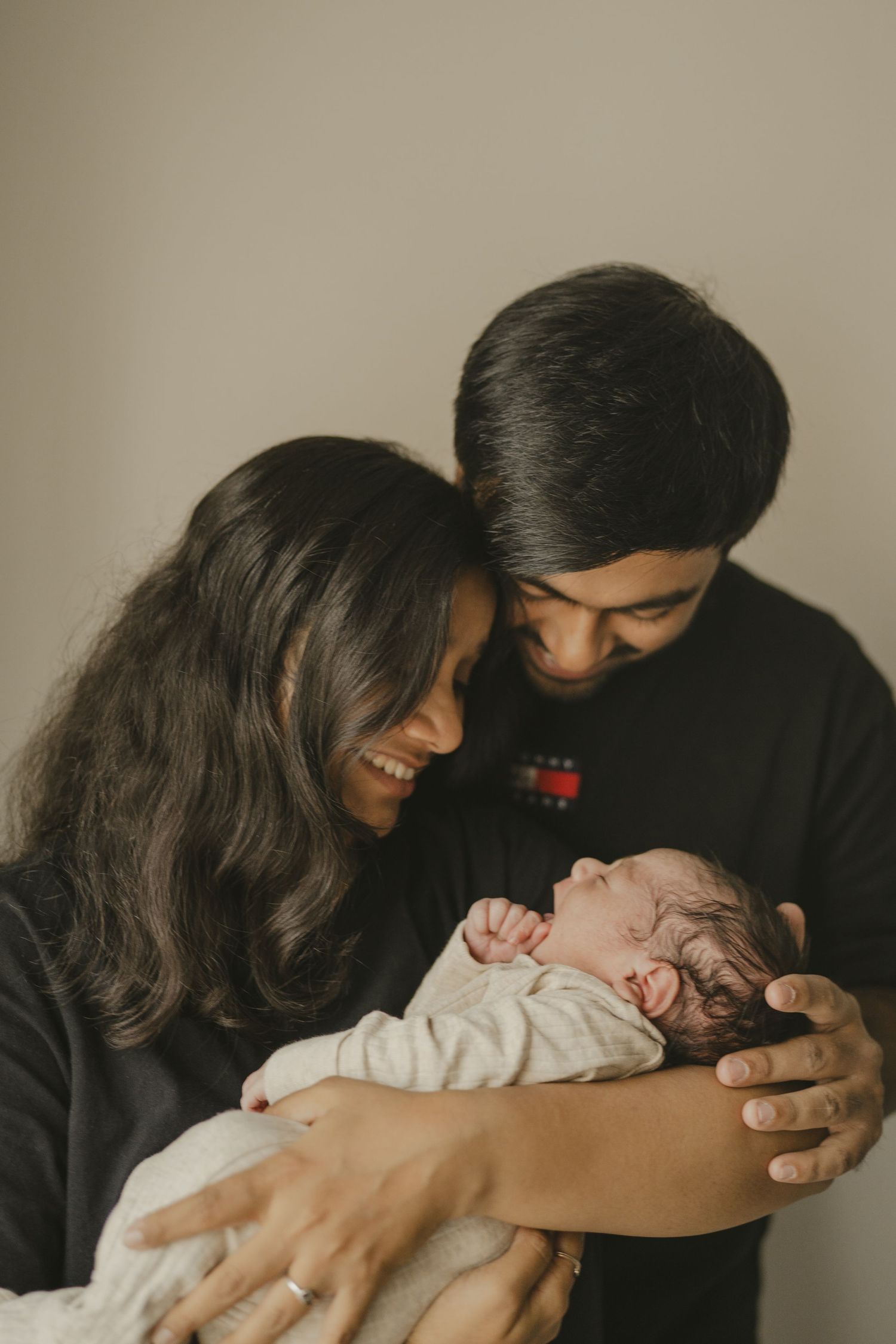Smiling parents in black outfits lovingly cradling their newborn baby together.
