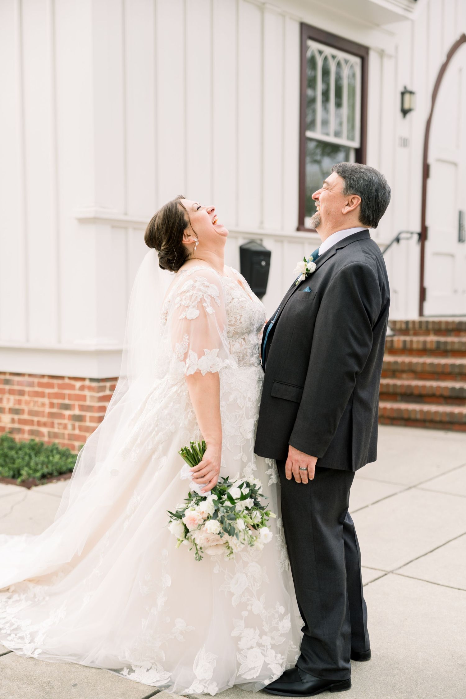 Bride and groom laughing joyfully together outside a white church on their wedding day.