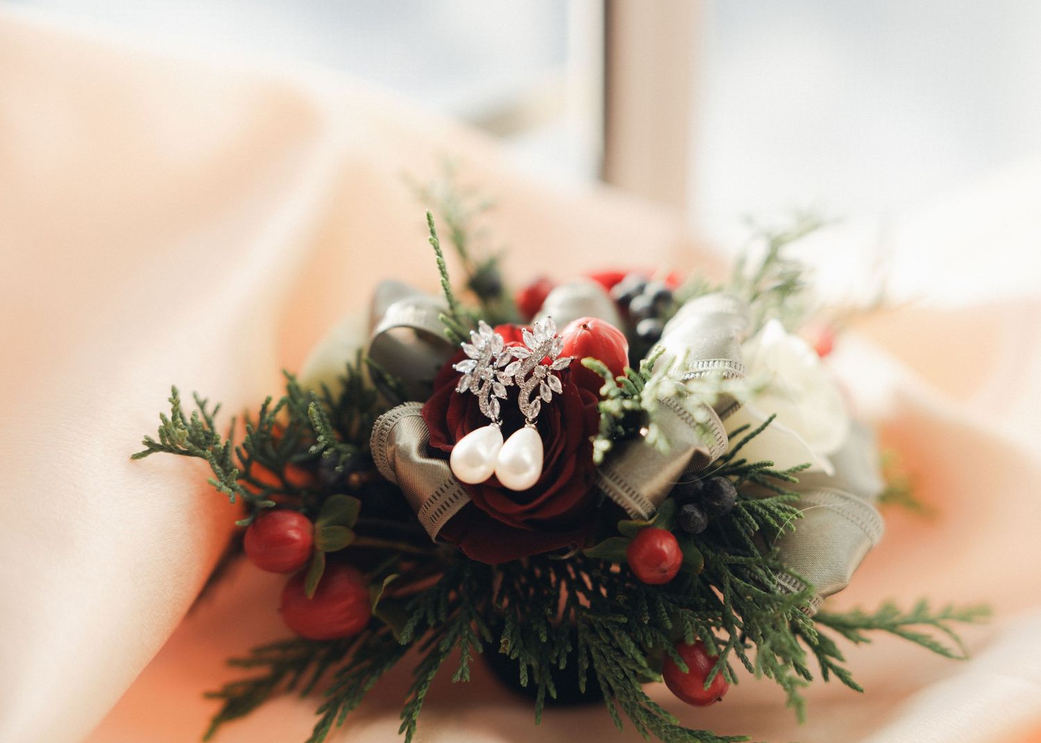 Winter wedding boutonniere with red berries, evergreen sprigs, white flower, and pearl pins.