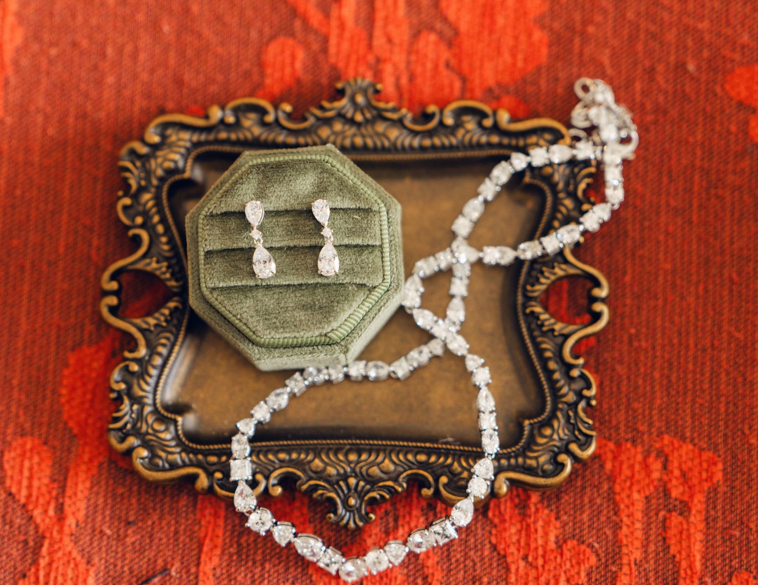 Elegant diamond drop earrings and tennis bracelet displayed on a vintage ornate jewelry tray.
