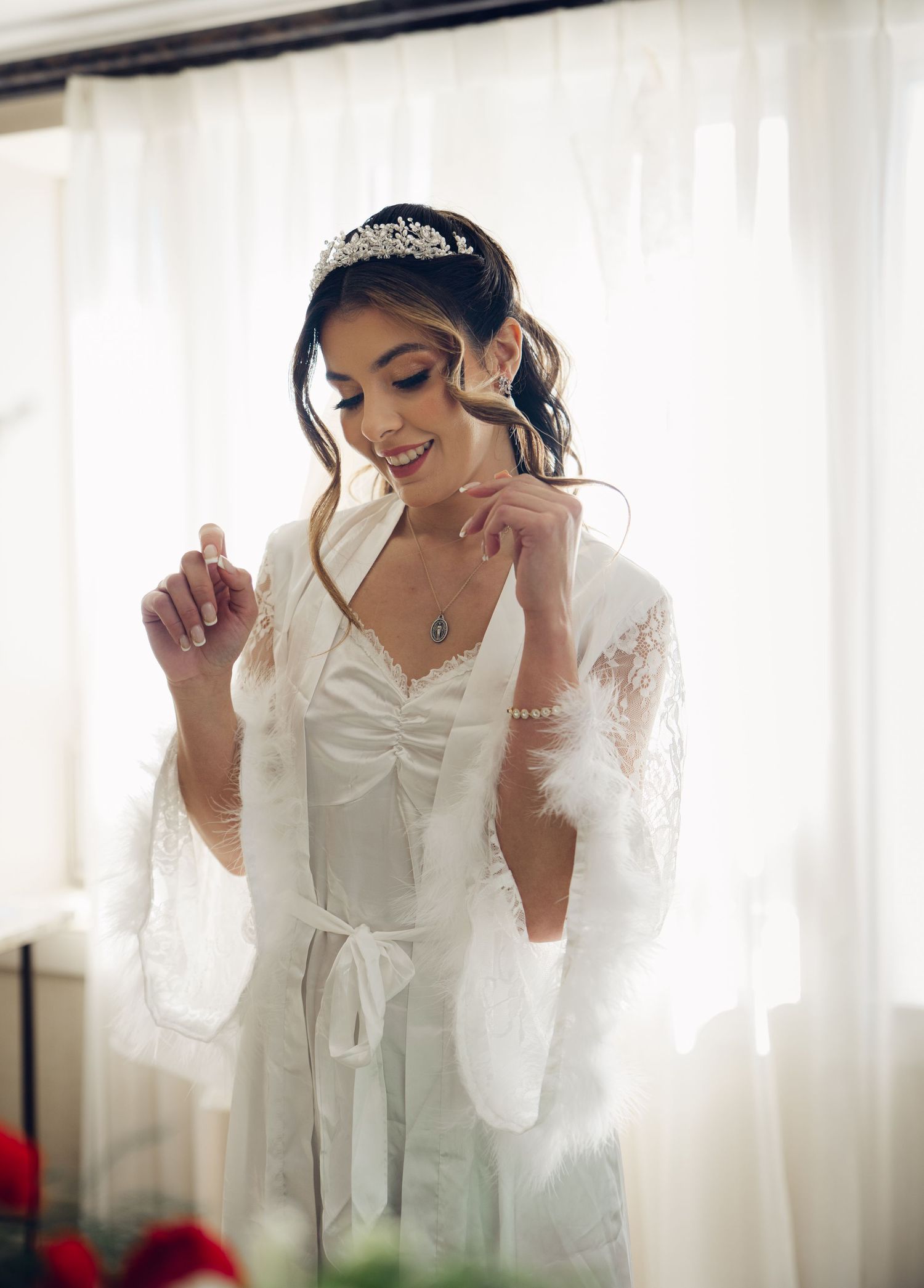 Smiling bride in white robe and tiara preparing on wedding morning.