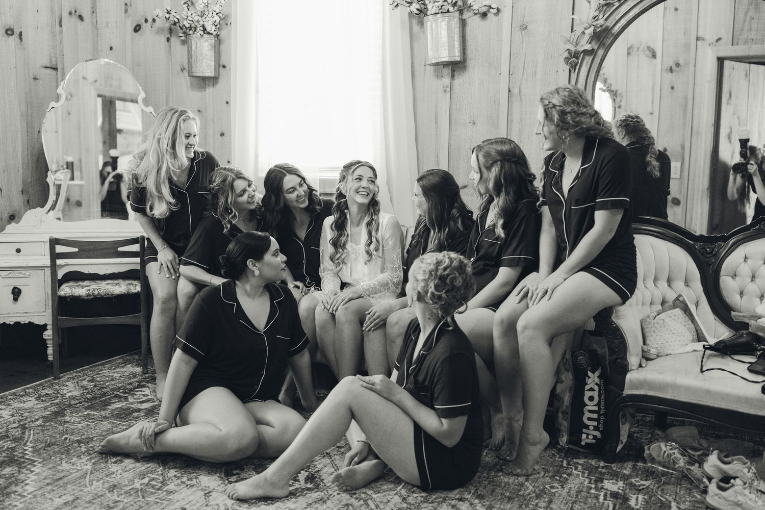 Bridesmaids in matching pajamas gather together laughing in a vintage decorated bridal suite before the wedding.
