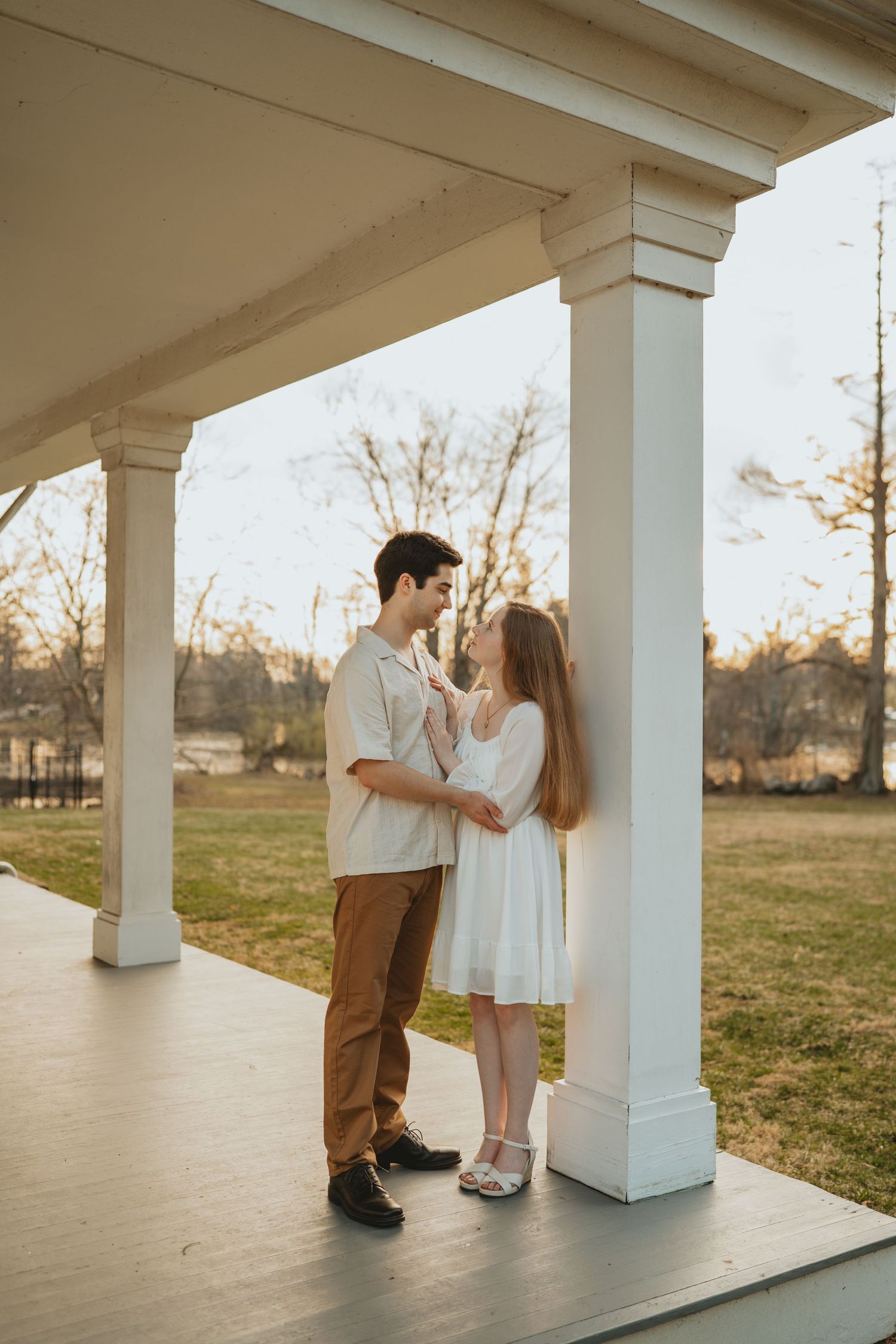 Young couple sharing a romantic moment on a rustic white porch at sunset.