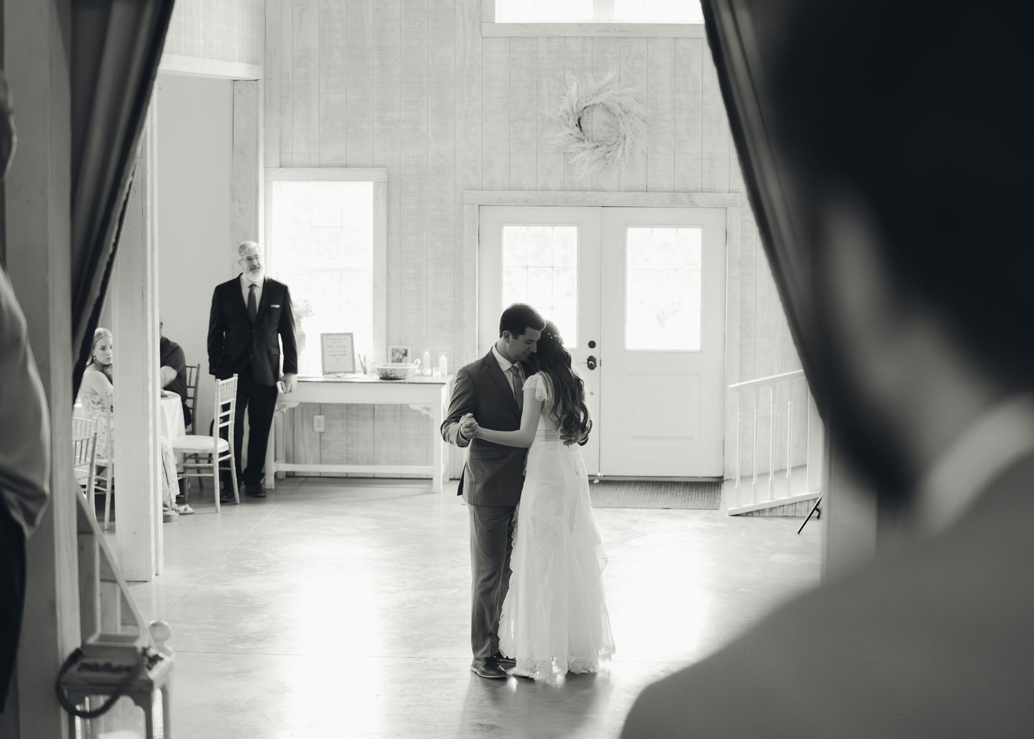 Black and white photo of bride and groom sharing first dance in elegant white wedding venue.