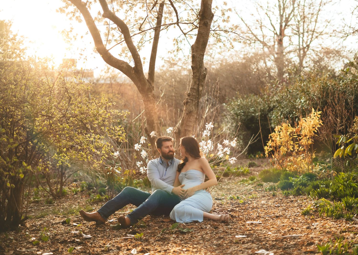 Expecting couple sitting together on the ground surrounded by autumn foliage in a warm golden sunset setting.