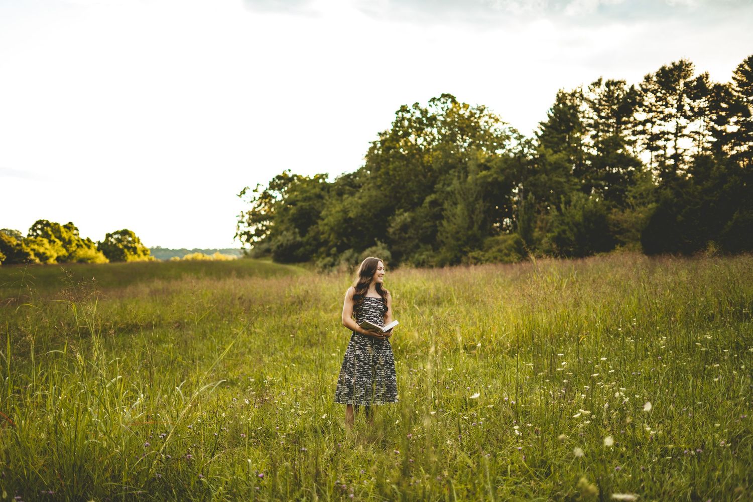 Young woman in floral dress standing alone in golden sunlit open field.