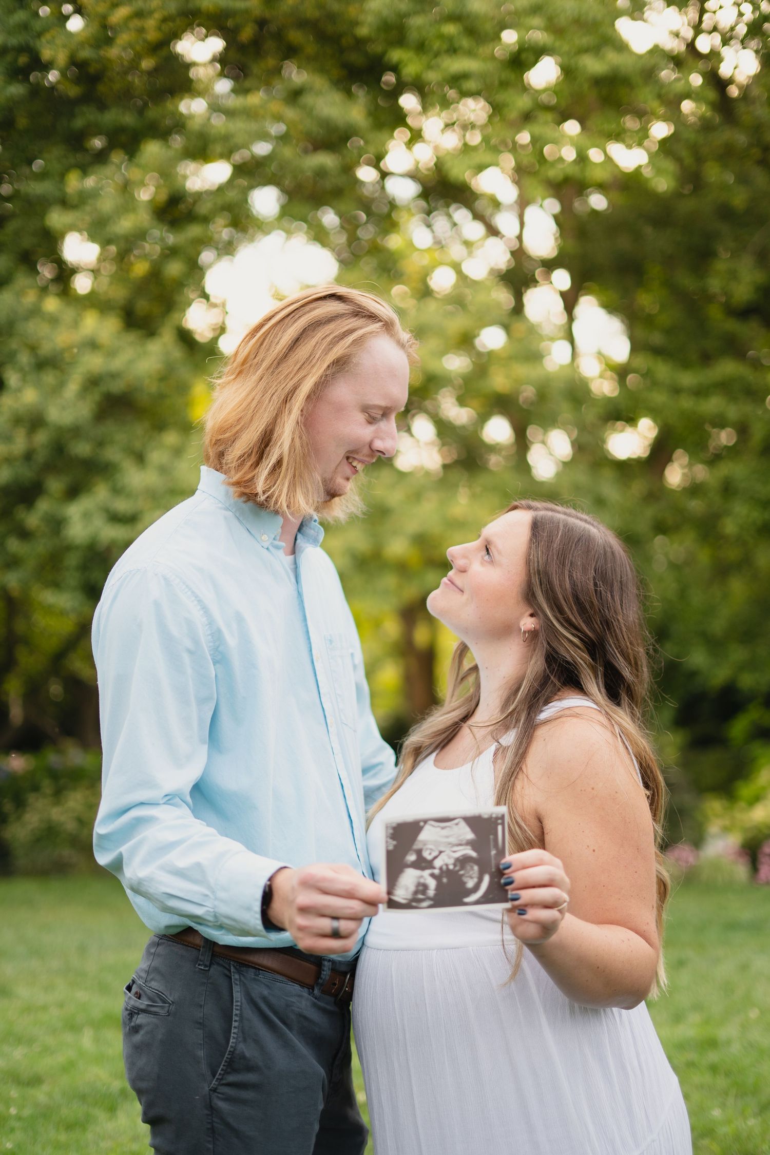 Smiling couple in garden holding ultrasound photo announcing pregnancy.