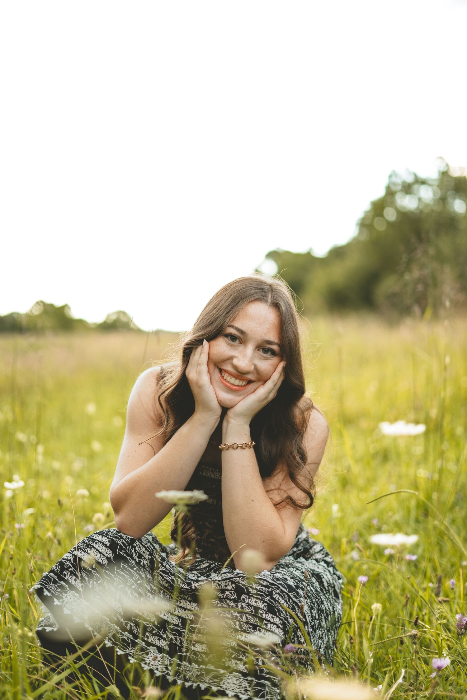 Happy young woman in floral dress lies in summer wildflower field smiling at camera.