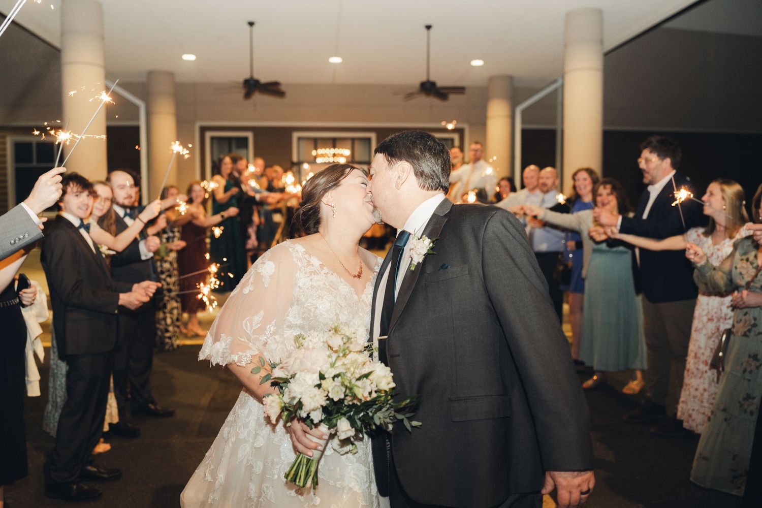 Bride and groom sharing romantic kiss during sparkler send-off with wedding guests.
