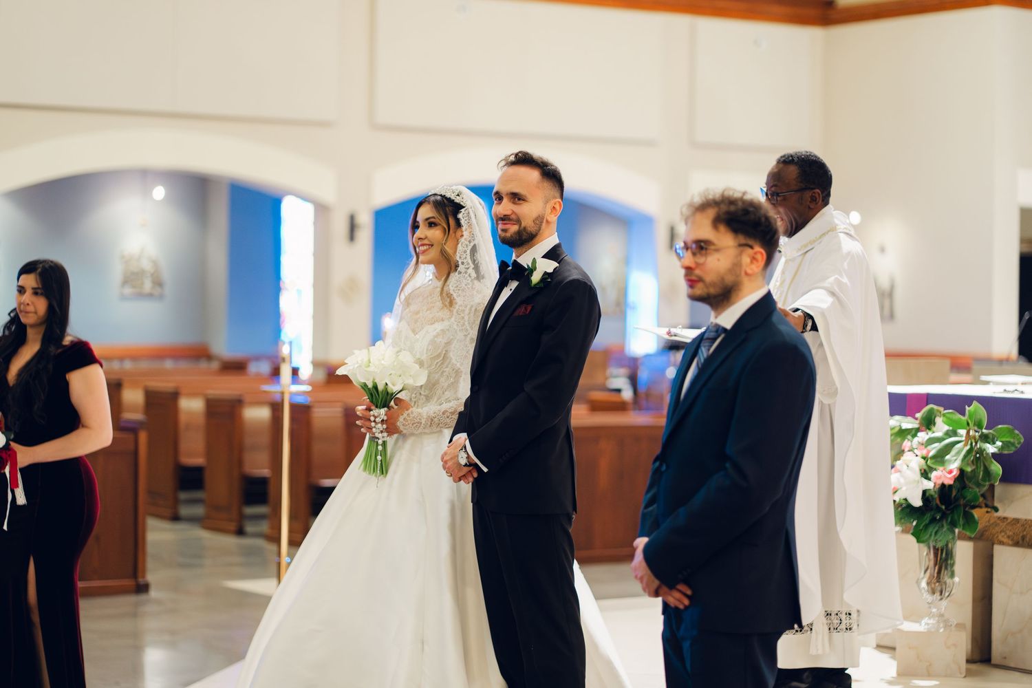 Bride in white gown and groom in navy suit standing at church altar during wedding ceremony.
