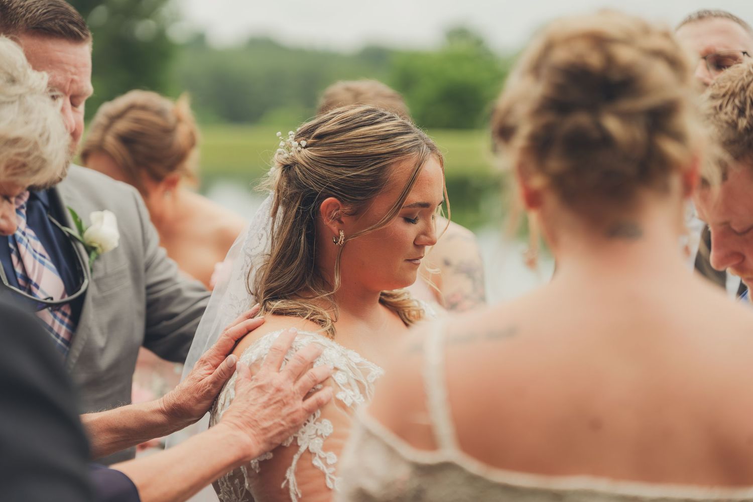 Bride surrounded by family and friends during an outdoor wedding ceremony, wearing a lace gown.