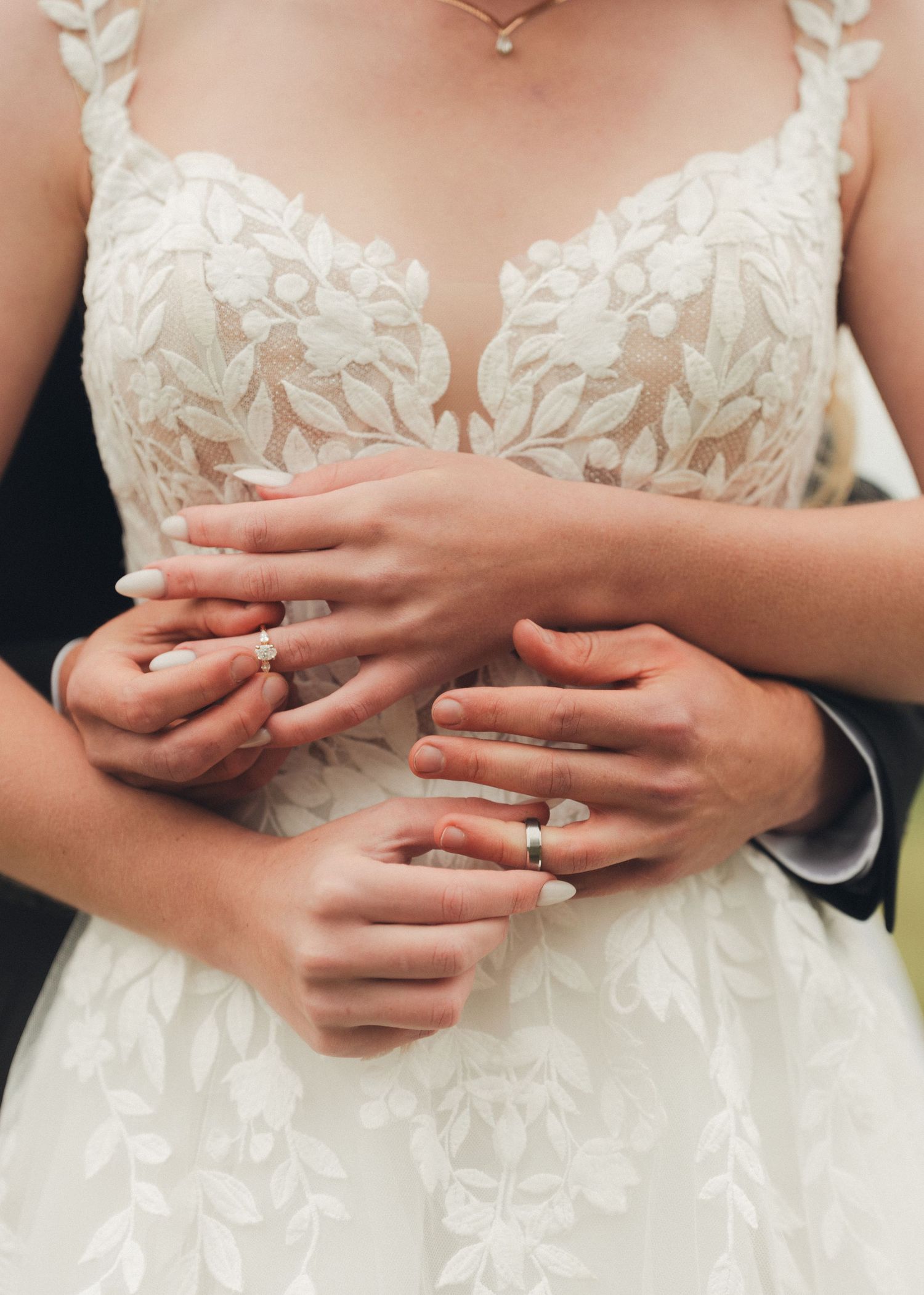 Close-up of bride and groom showing their wedding rings with hands clasped over the brides lace gown.