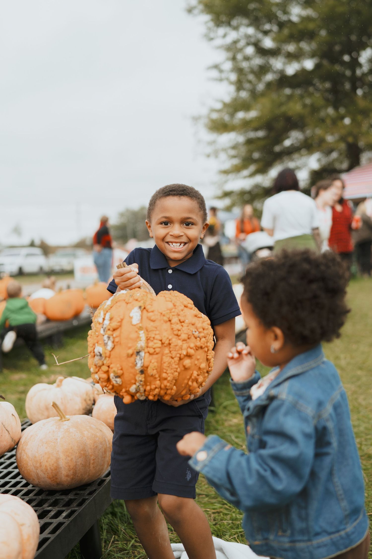 Joyful boy holding a large bumpy pumpkin at an outdoor fall pumpkin patch.