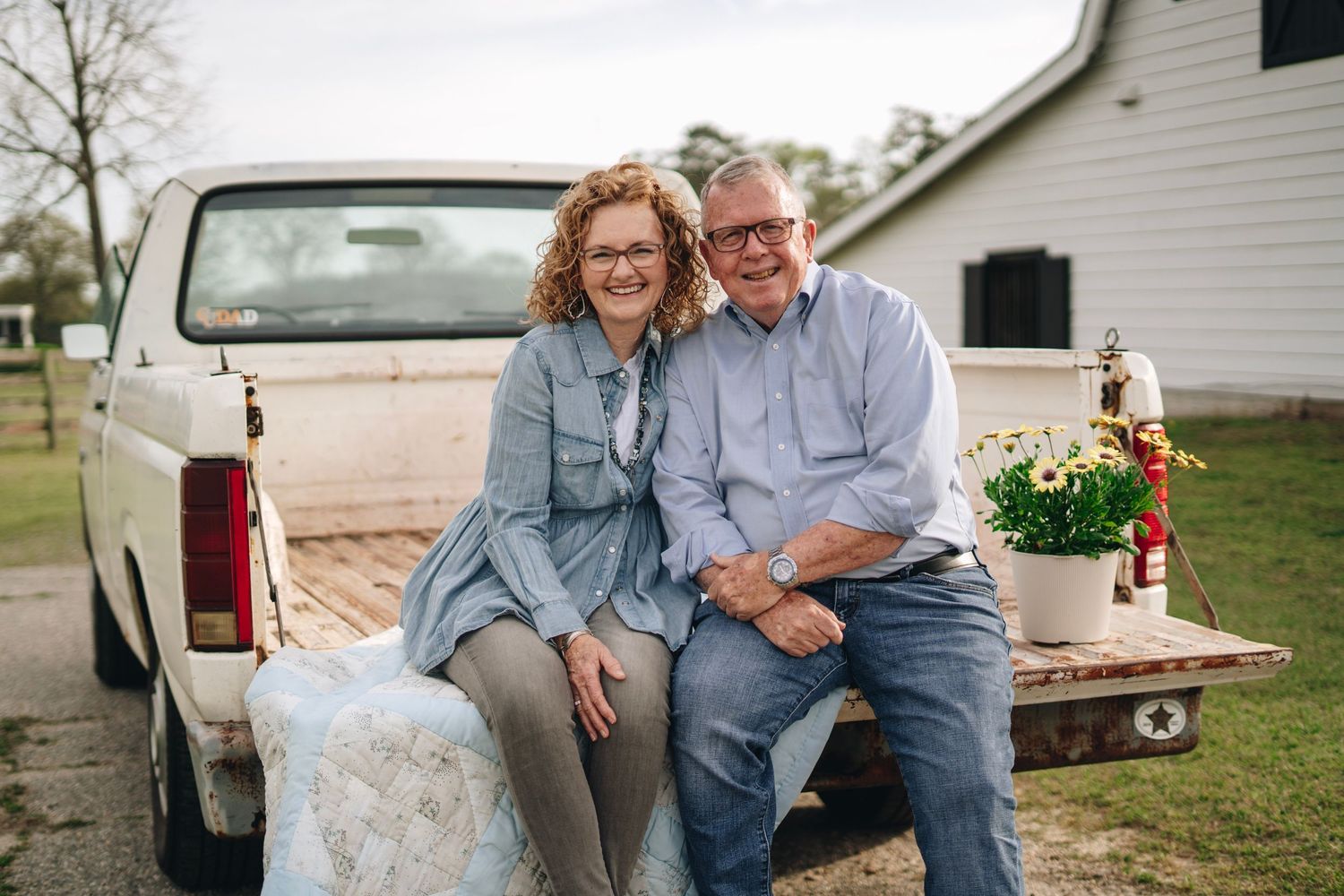 Happy older couple sitting together on tailgate of vintage white pickup truck on a farm.