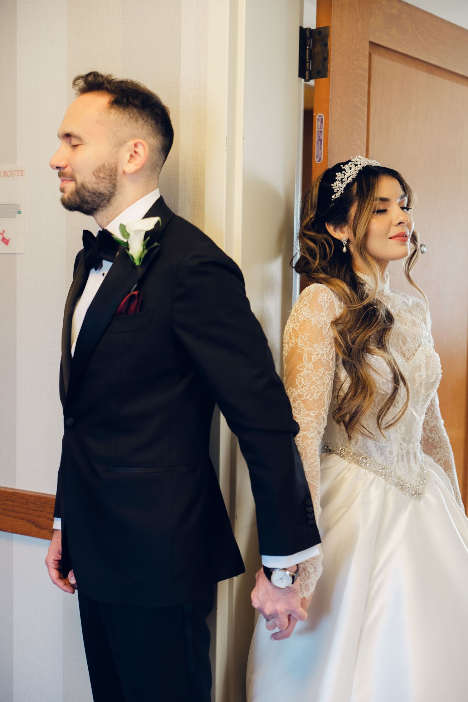 Bride and groom holding hands around a door in a romantic first look wedding moment.