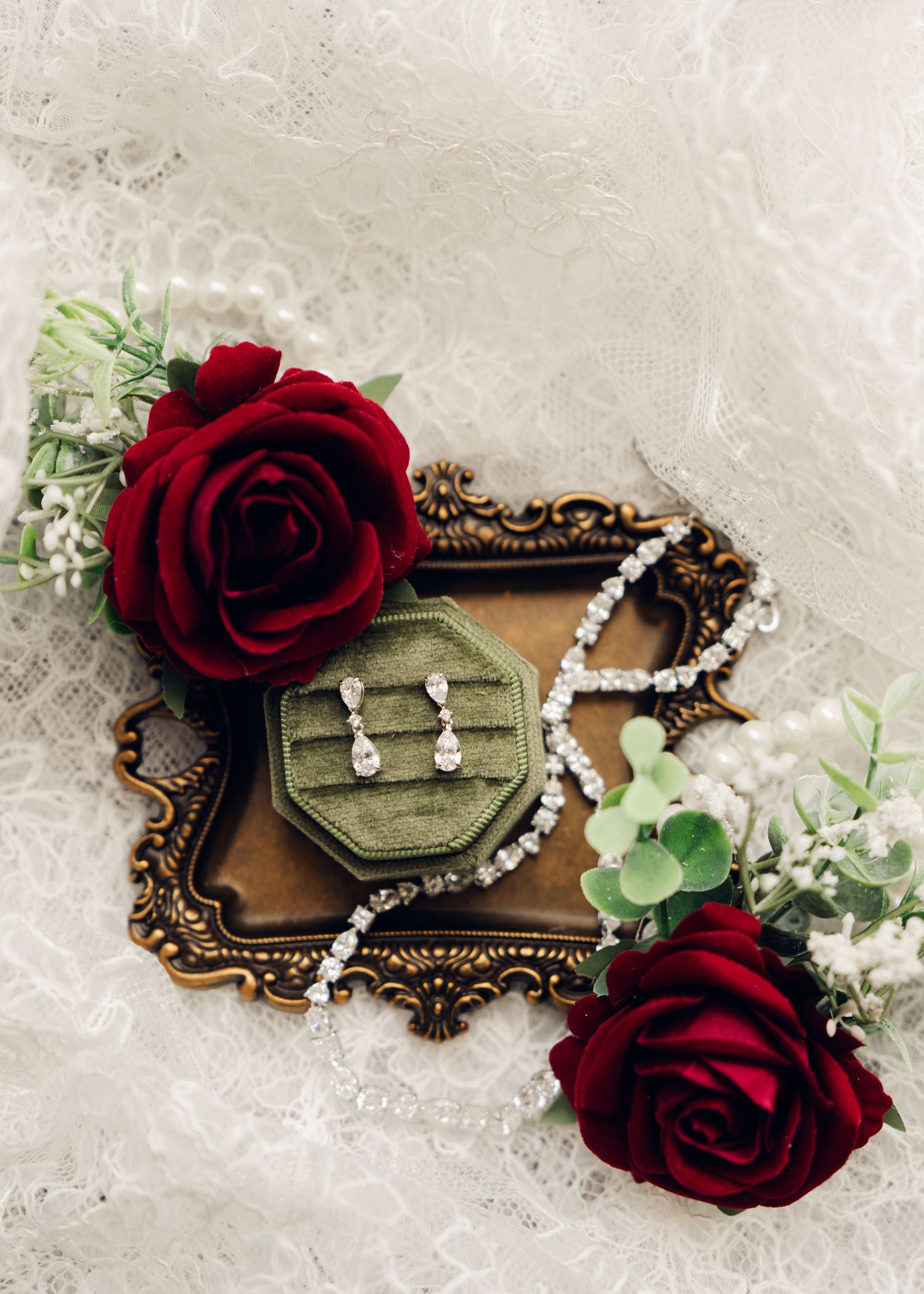 Bridal jewelry flat lay with diamond earrings, crystal necklace, and red roses on vintage tray.