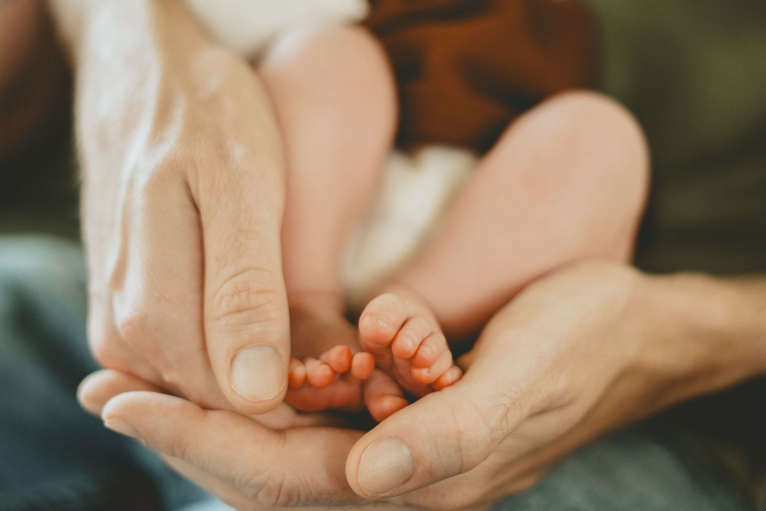 Close-up of adult hands tenderly cradling tiny newborn baby feet and toes.