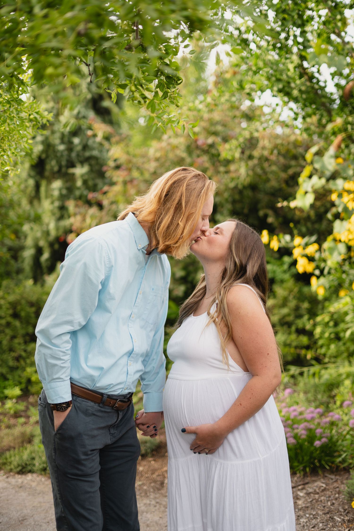 Pregnant couple sharing a kiss in a lush green garden setting.