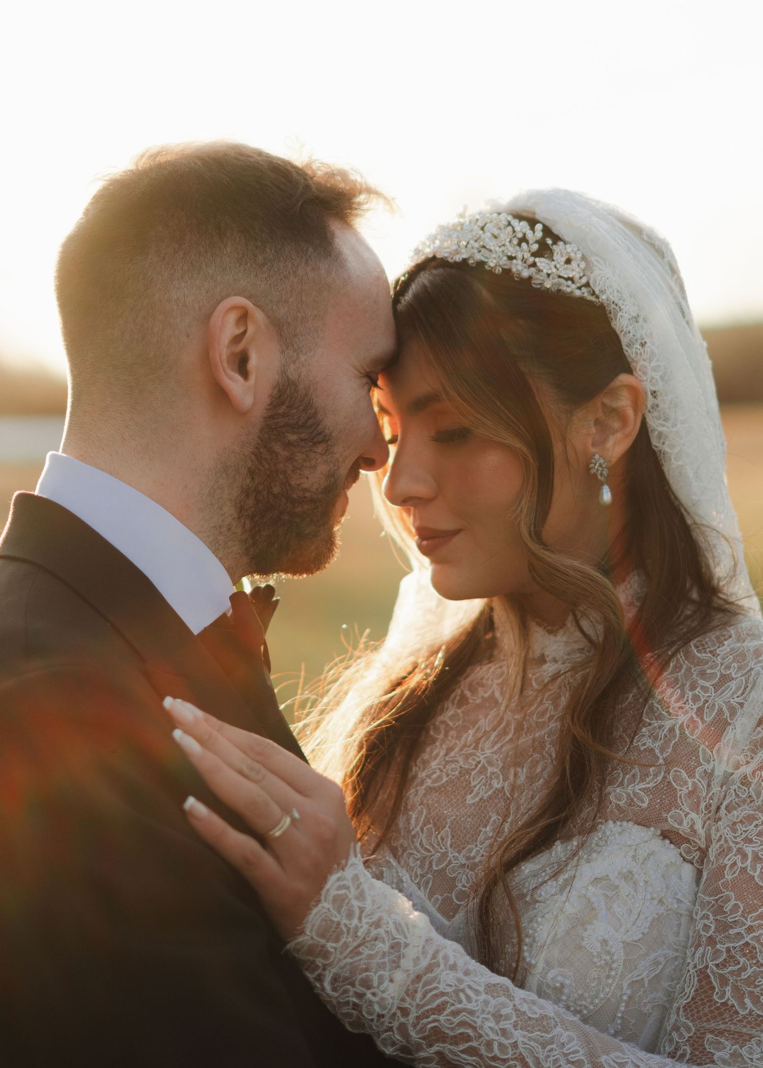 Bride and groom sharing an intimate moment in golden sunset light, bride wearing lace gown and veil.
