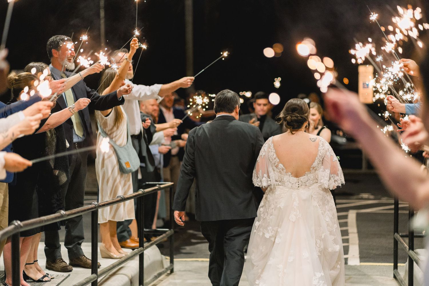 Bride and groom walking through sparkler exit tunnel at night wedding celebration.