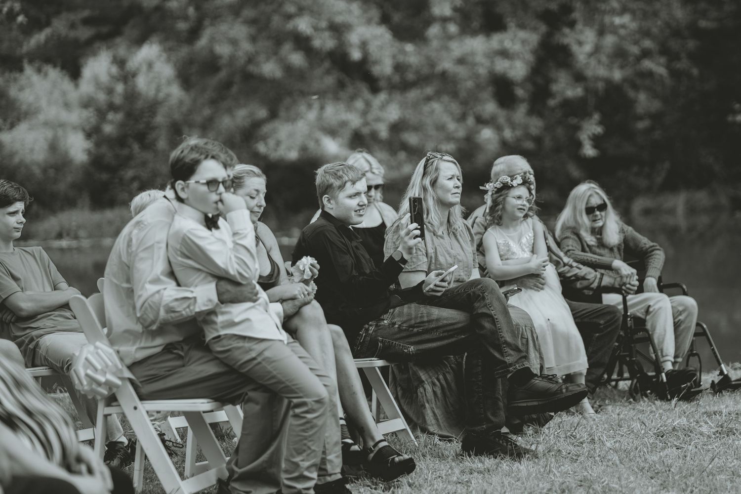 Black and white photo of wedding guests seated in chairs attentively watching an outdoor garden ceremony.