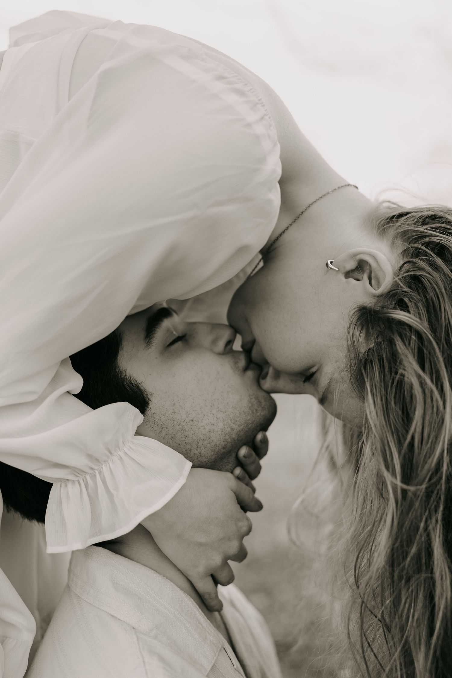 Black and white photo of a couple sharing an intimate upside-down kiss outdoors.