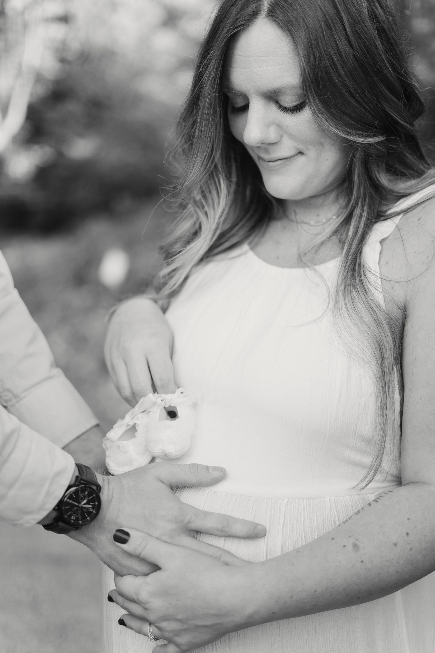 Black and white photo of couple holding baby shoes on pregnant belly.