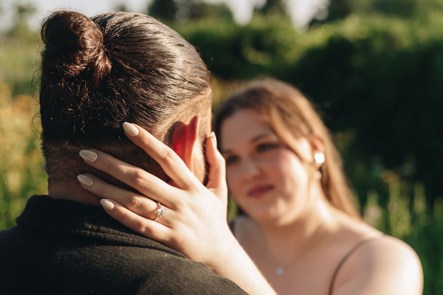 Close-up of engaged woman placing hand on partners neck showing diamond engagement ring outdoors.