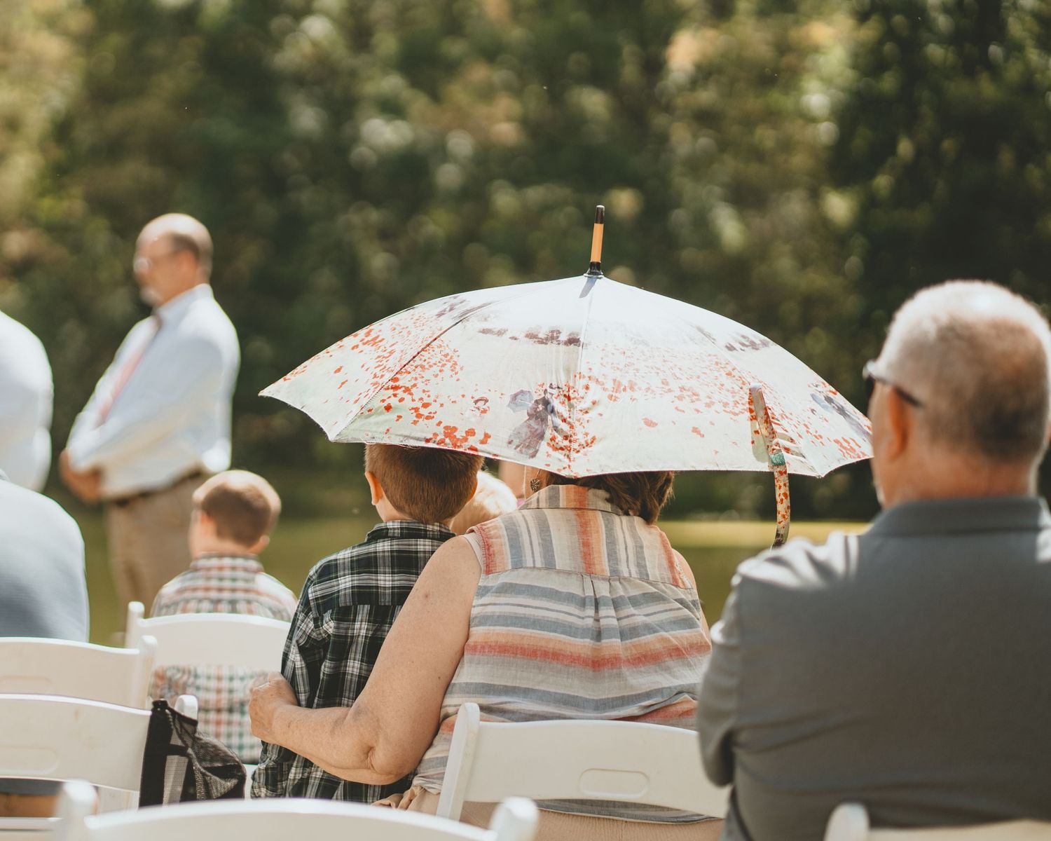 Wedding guest shades herself with a floral umbrella during an outdoor garden wedding ceremony.