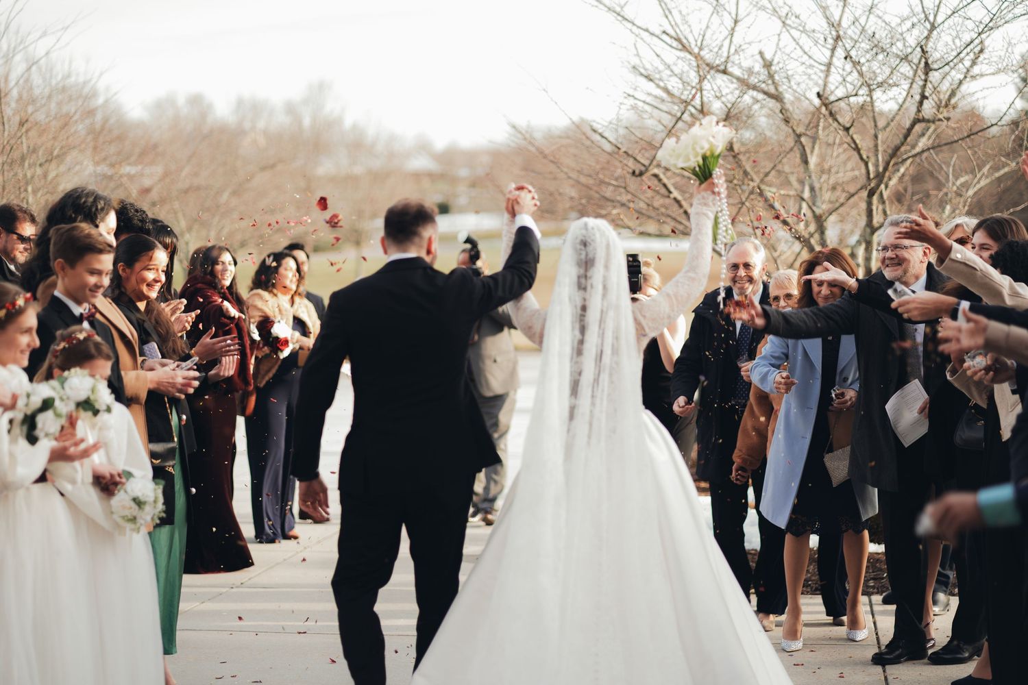 Newlywed couple celebrates joyfully walking back down the aisle surrounded by cheering wedding guests outdoors.