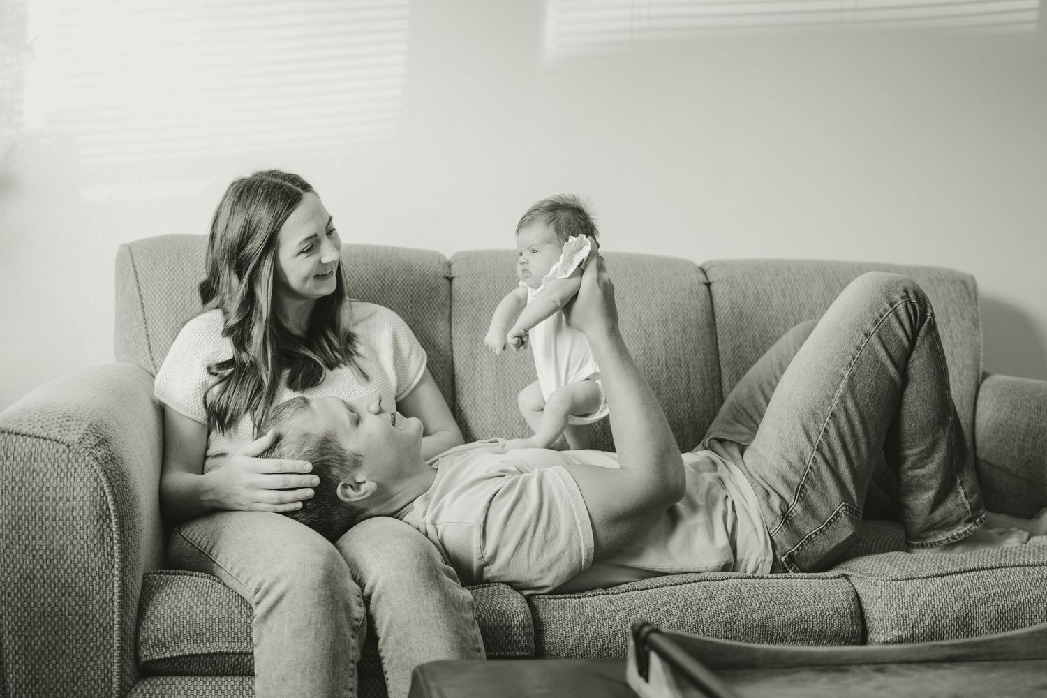 Black and white photo of couple relaxing on sofa with their newborn baby.