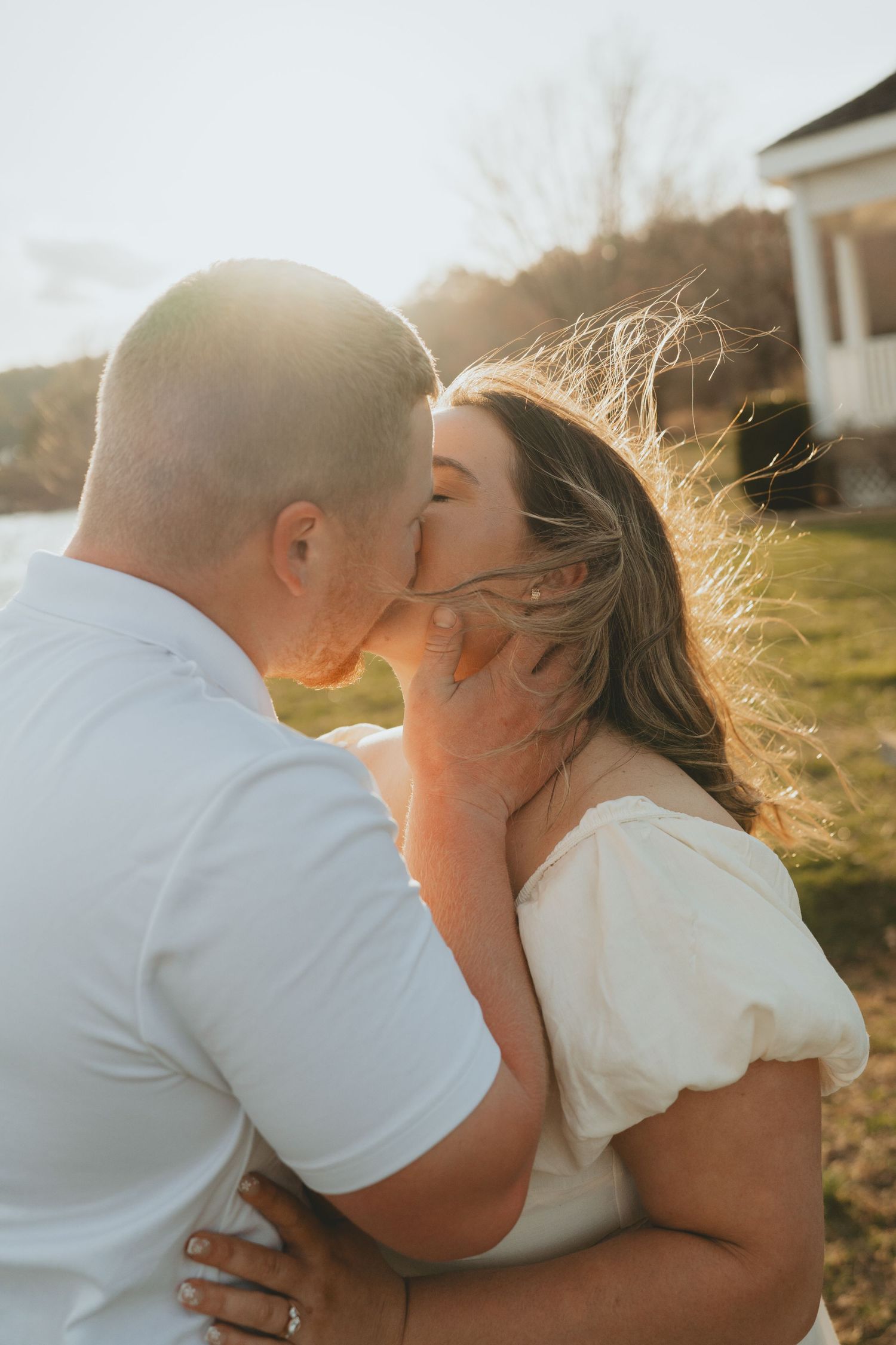 Couple sharing a tender kiss outdoors at golden hour with warm sunlight glowing behind them.