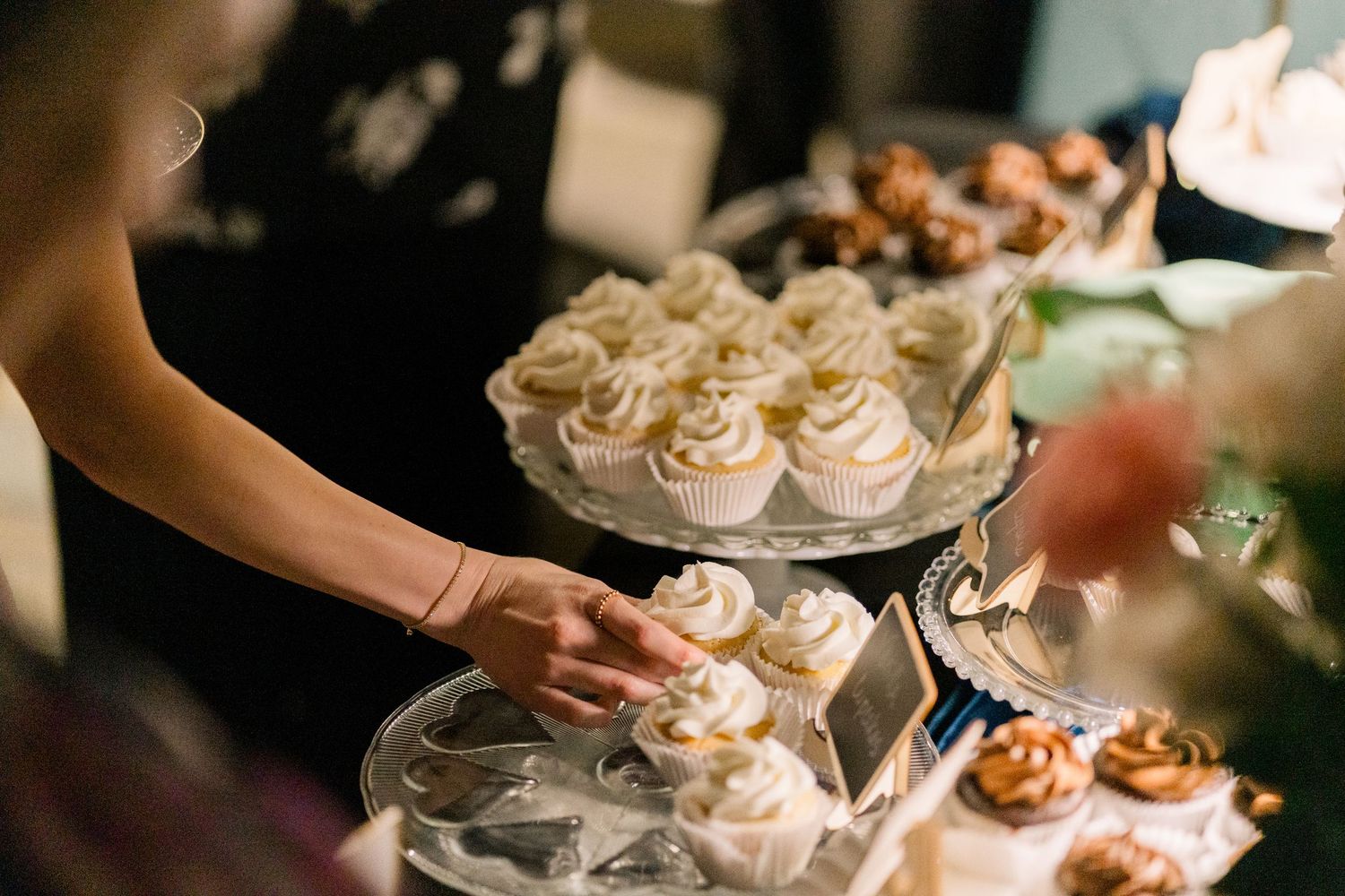 Guest selecting vanilla cupcake from tiered dessert display at wedding reception.
