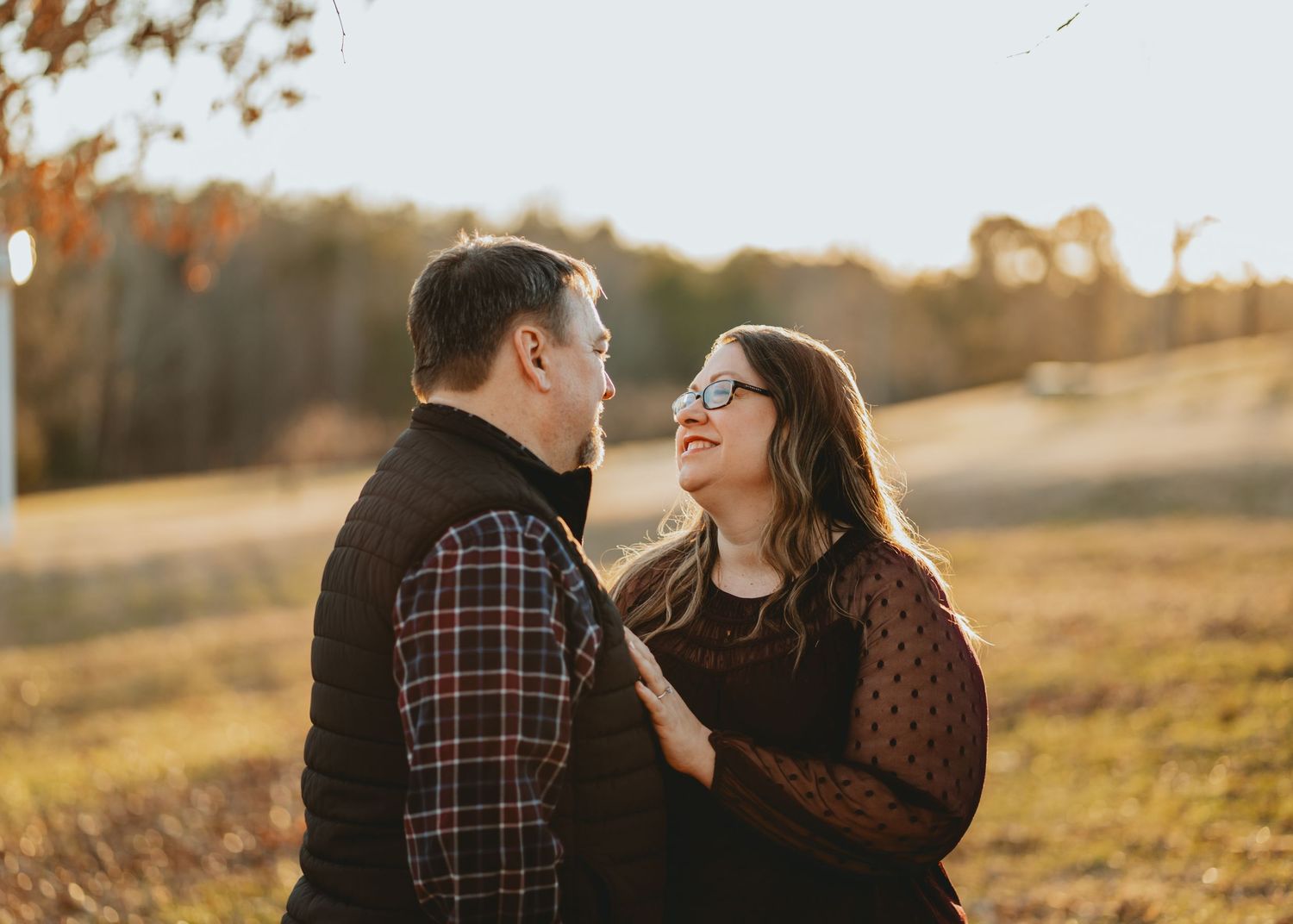 Couple smiling at each other in a golden autumn field during engagement photography session.