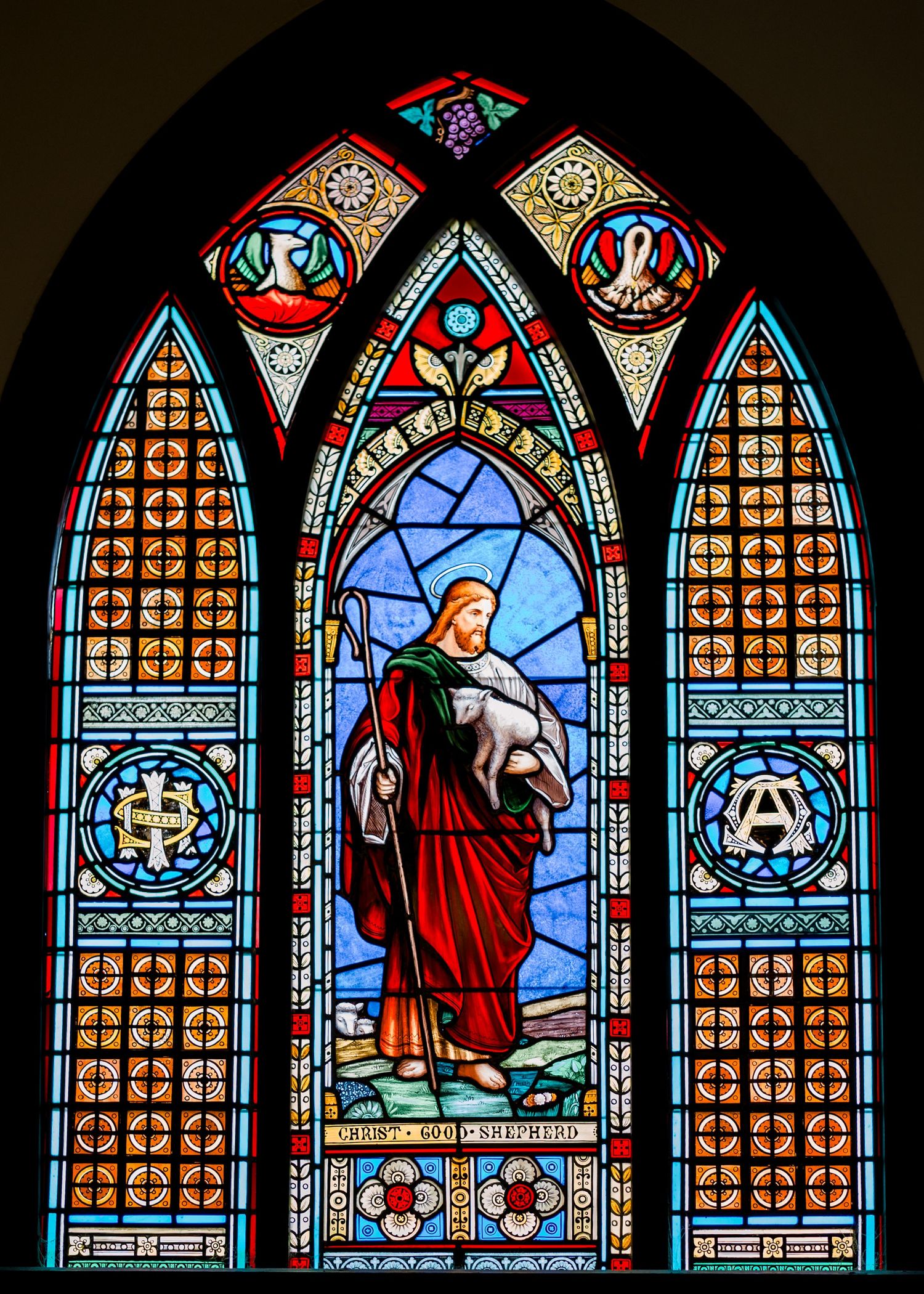 Beautiful stained glass church window depicting Christ the Good Shepherd in colorful detail.