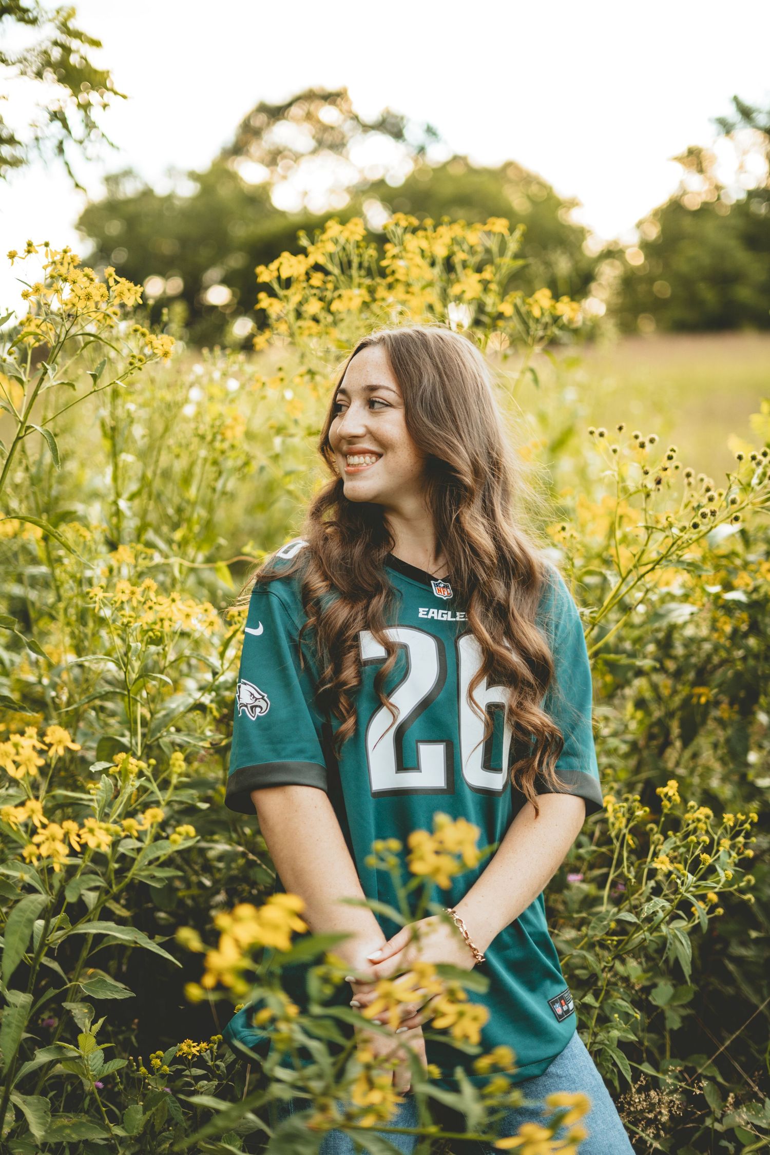 Young woman in Eagles jersey smiling among yellow wildflowers in a sunlit field.
