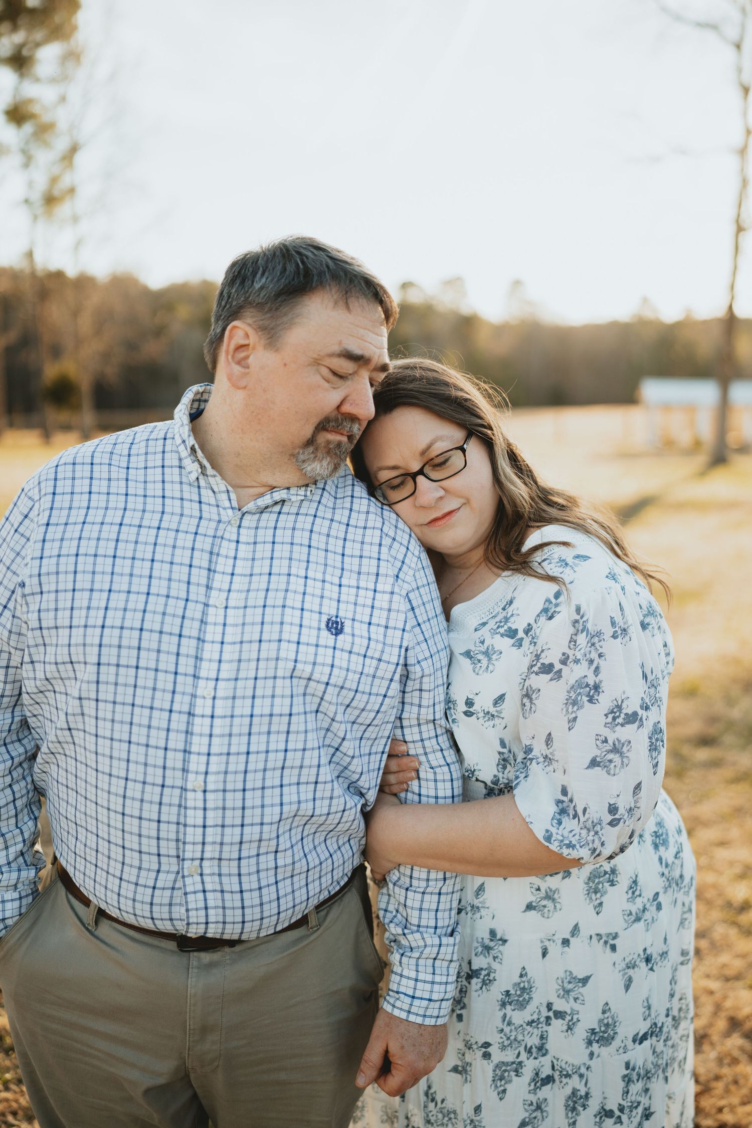 Woman resting her head on a man's shoulder in a sunny field.