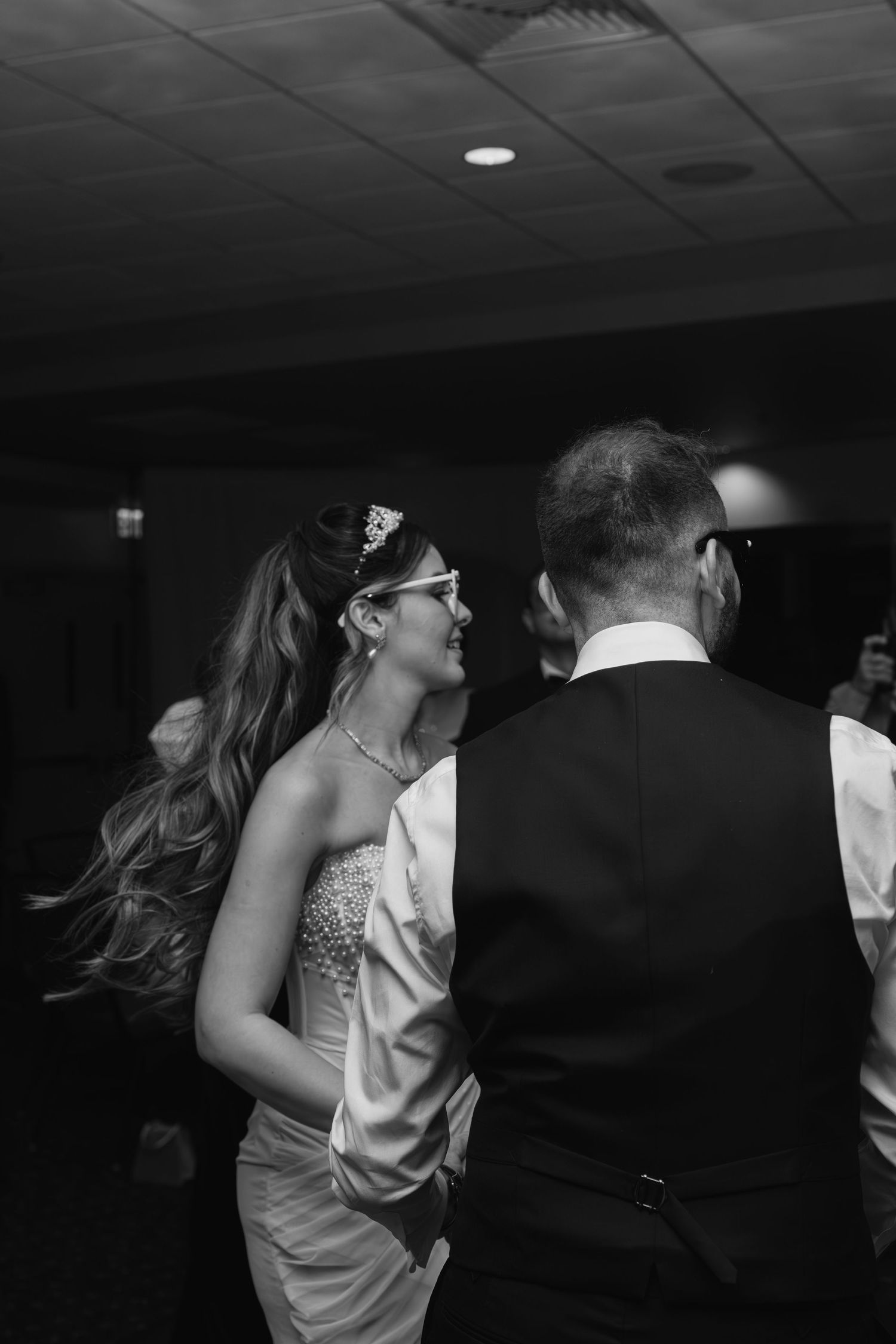 Black and white photo of bride dancing with older gentleman at wedding reception, bride wearing beaded gown and tiara.