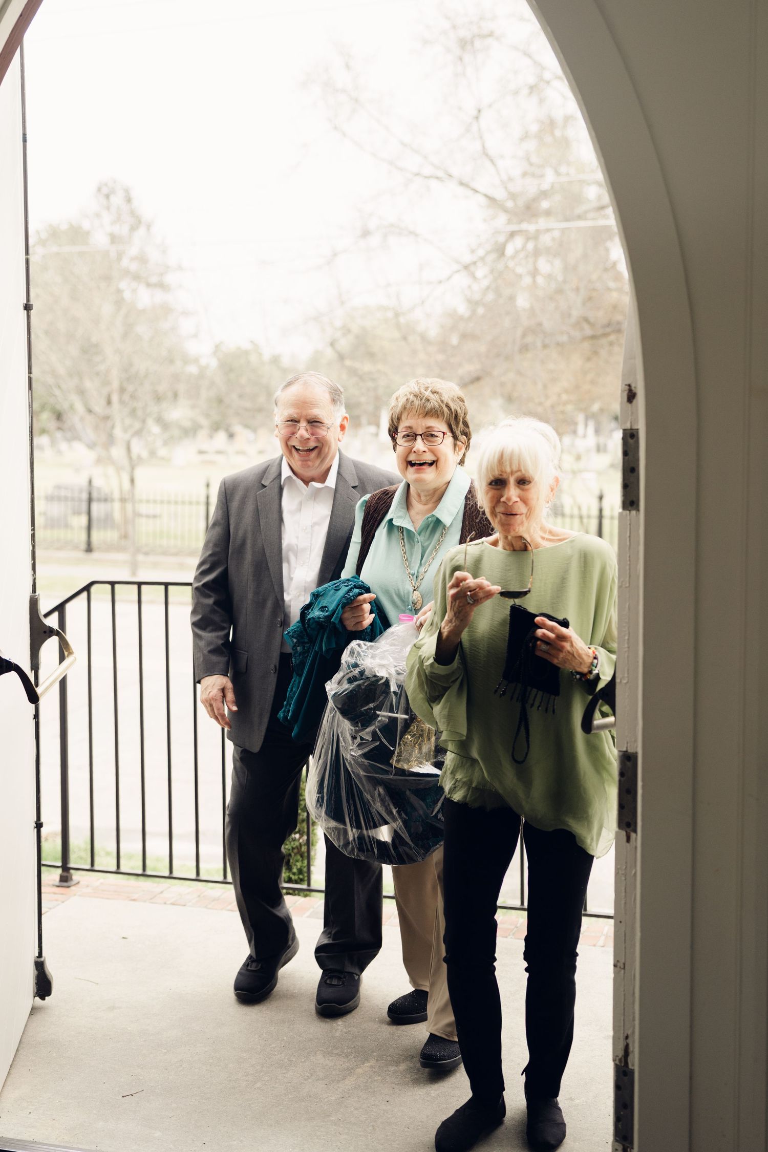 Three smiling elderly guests arriving at wedding venue through arched doorway.